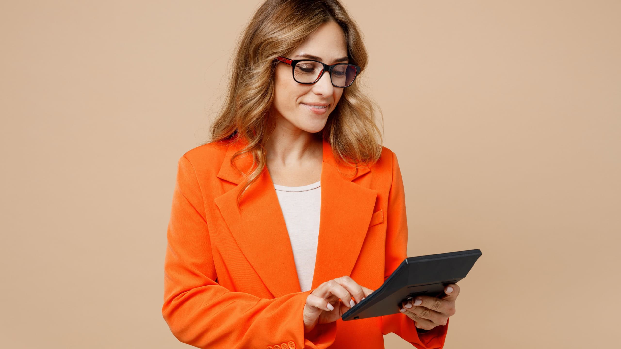 Young smiling fun successful employee business woman corporate lawyer 30s wear classic formal orange suit glasses work in office hold in hand using calculator isolated on plain beige background studio