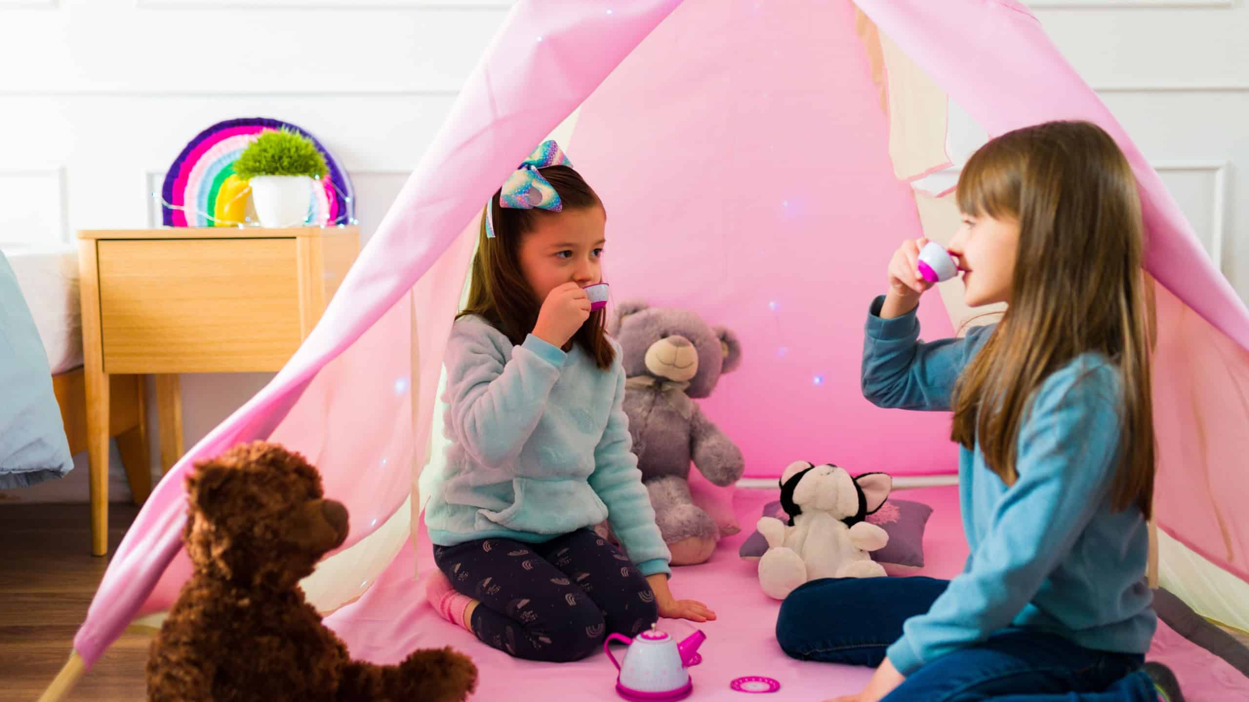 Beautiful little girls drinking tea and having fun with toys while having a fun play date together in a pink tipi