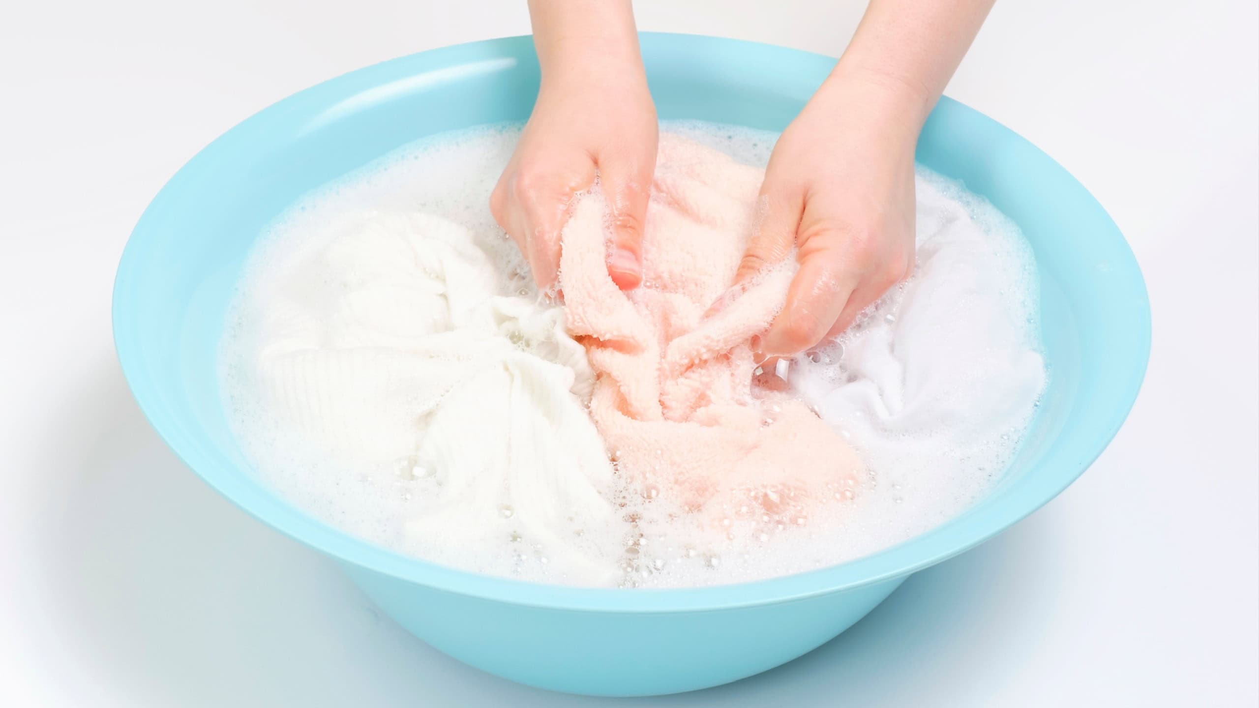 Female hands washing pink towels in basin on a white background.