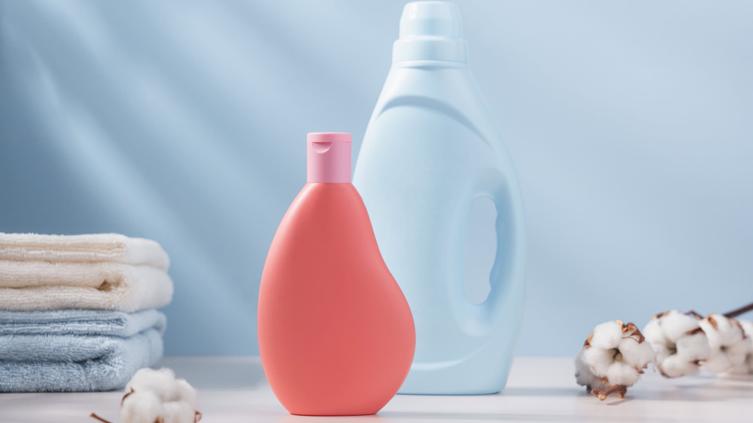 Blue and pink plastic bottle of laundry detergent with cotton towels and branch of cotton in the background. Delicate wash concept