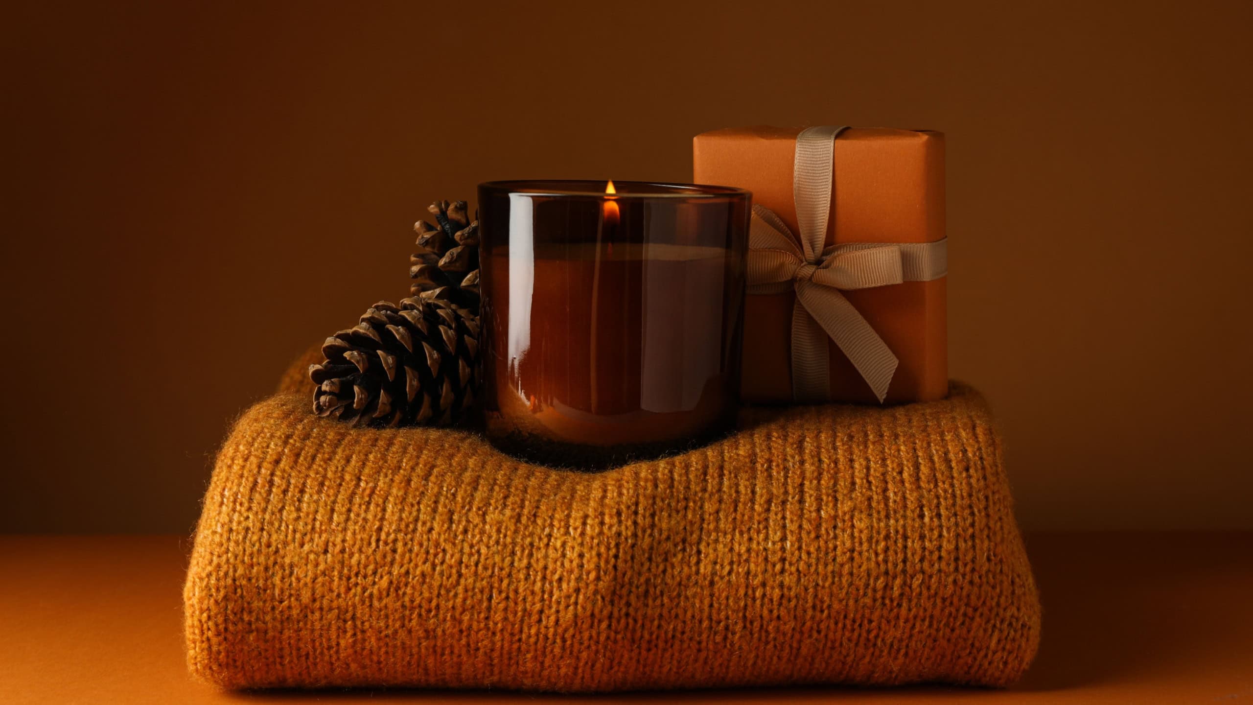 Candle, cones and box on sweater on orange background