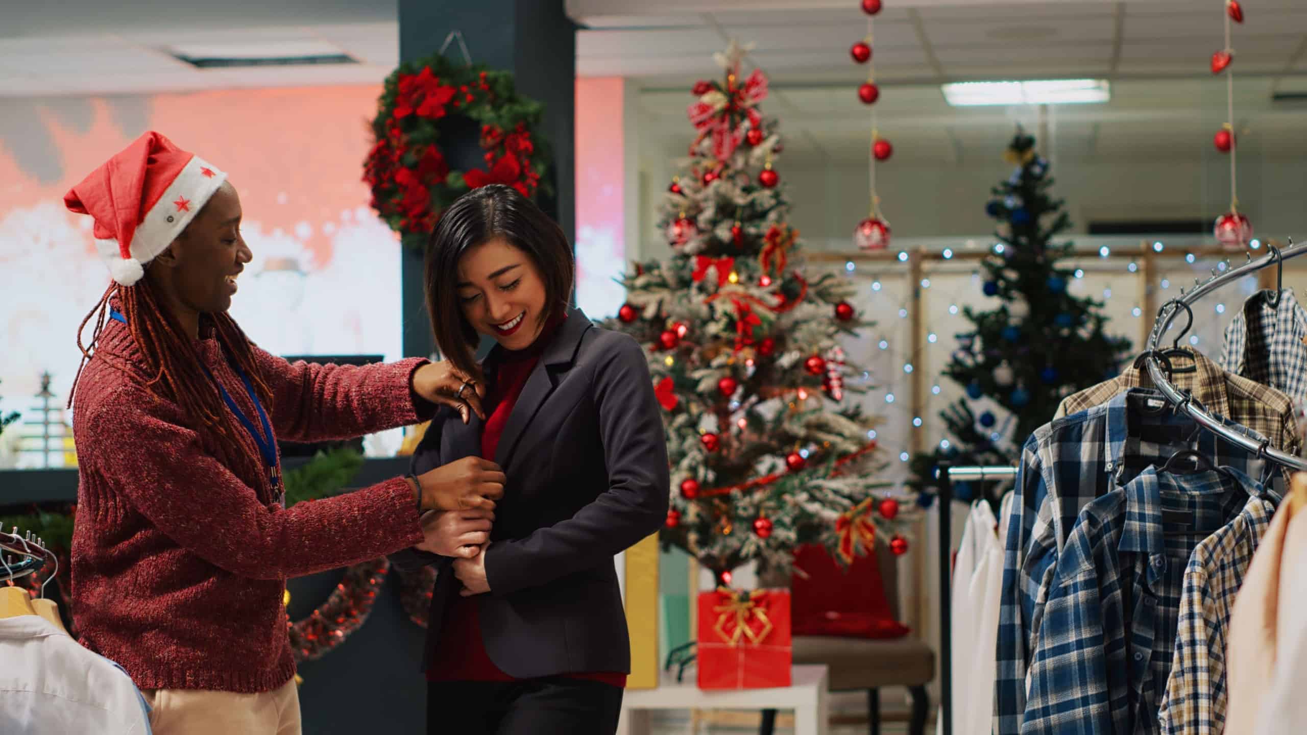 Businesswoman doing pirouette while trying elegant blazer, asking worker for opinion before buying it. Client and employee in xmas adorn clothing shop during winter holiday season