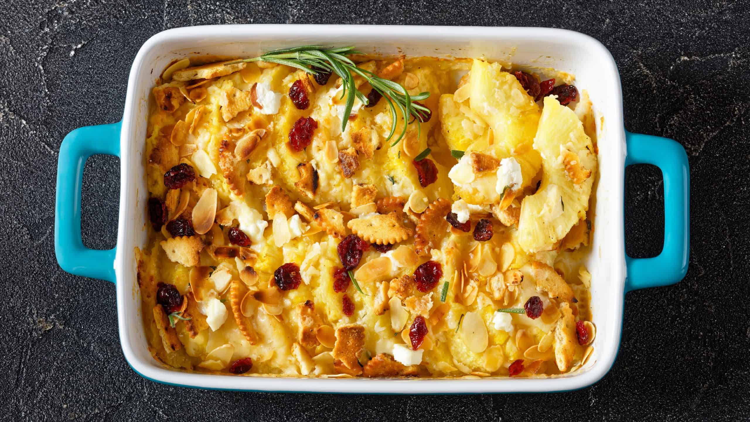 Pineapple half-moon rings holiday casserole with cranberries, crackers, almond and cheese in baking dish on concrete table, horizontal view from above, flat lay, close-up