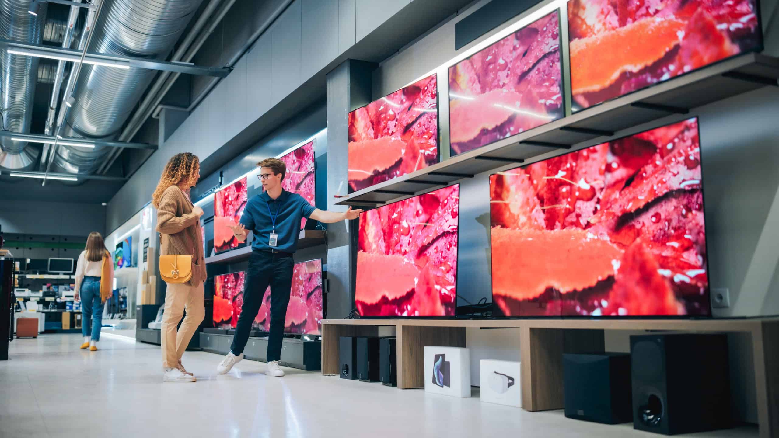 Hispanic Woman Having a Conversation with Home Electronics Store Associate. Young Multiethnic Customer Pursues Cutting-Edge TV Technology. Shopper Examining Modern Television Selection in a Showroom