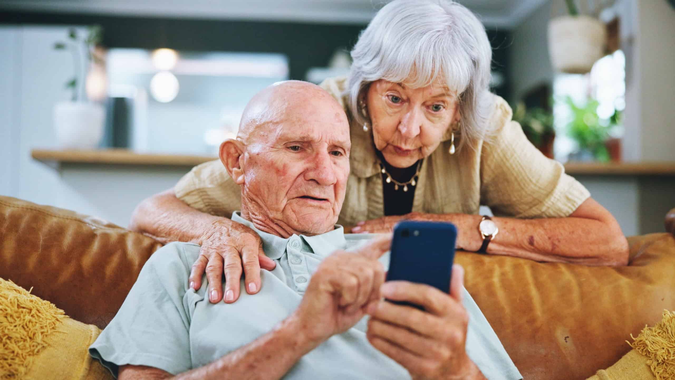 Senior couple, phone and search on couch for hug, choice and help with video, download and confused in home. Elderly woman, man and smartphone on sofa in lounge with thinking for post on social media