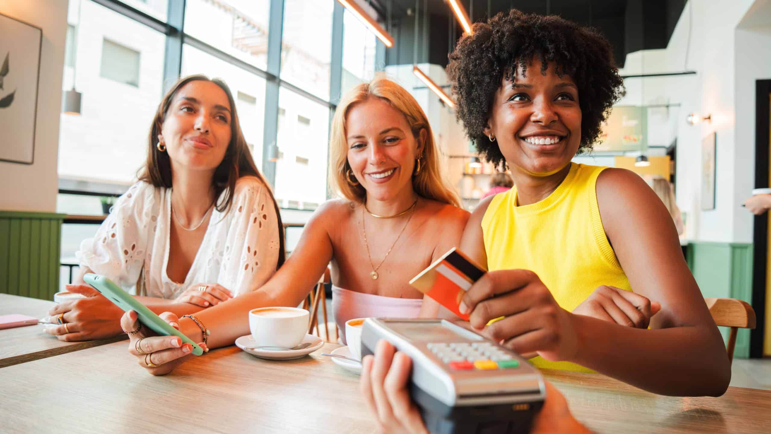 A cheerful young African American woman is settling her bill with a contactless creditcard at a restaurant. She smiles as she hands over her credit card to complete the payment with the cashier. High