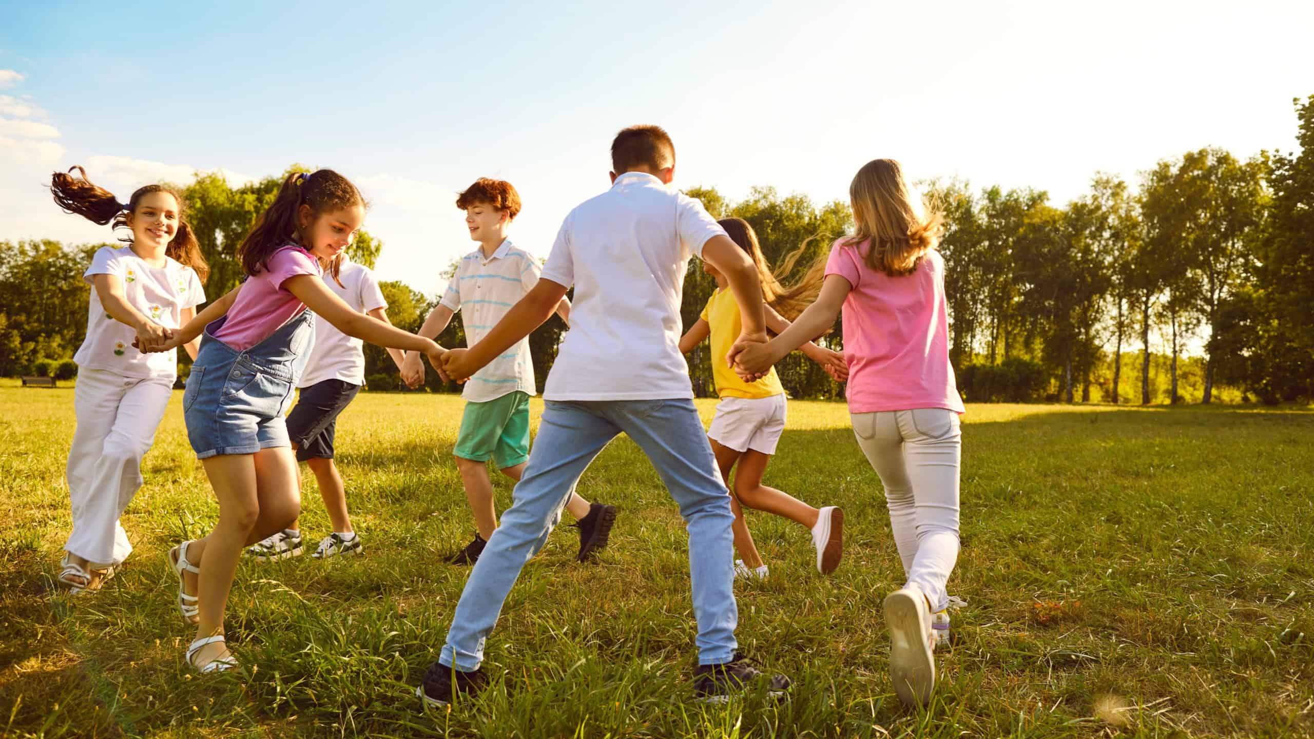 Group of a kids friends playing outside in the park standing in a circle and holding hands. Happy children playing games and having fun outdoor on a sunny summer day in casual clothes.