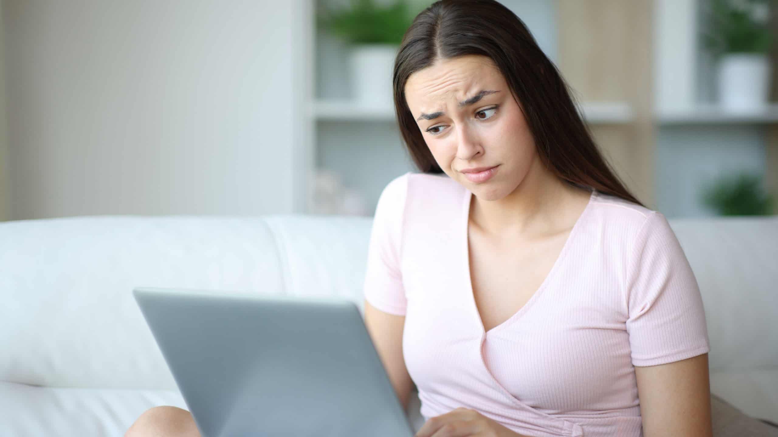 Suspicious woman using laptop sitting on a couch in a house