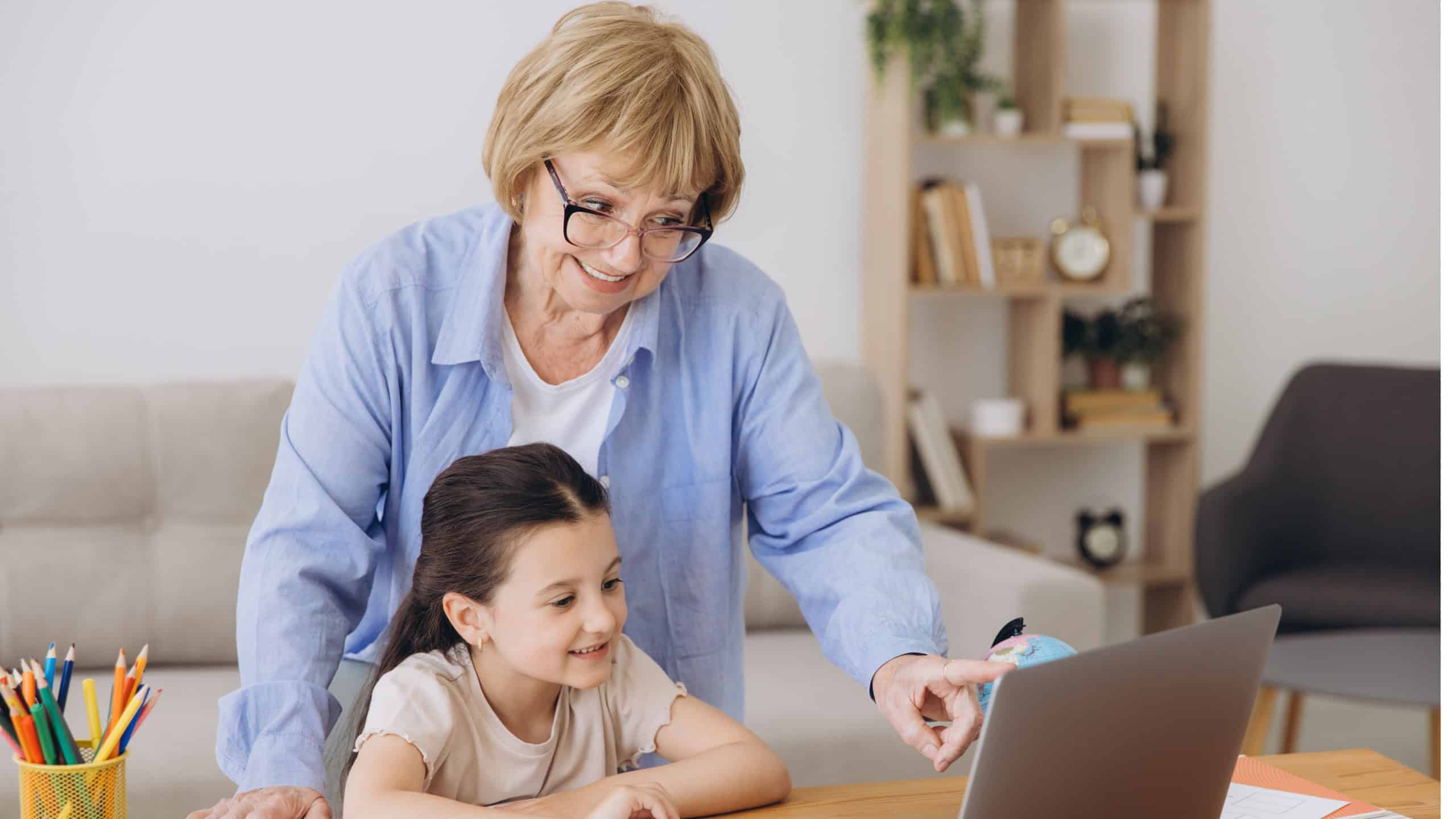 Happy grandma helping adorable preschool granddaughter school kid with homework task. Positive school pupil girl and granny reading learning book at laptop together, enjoying education at home