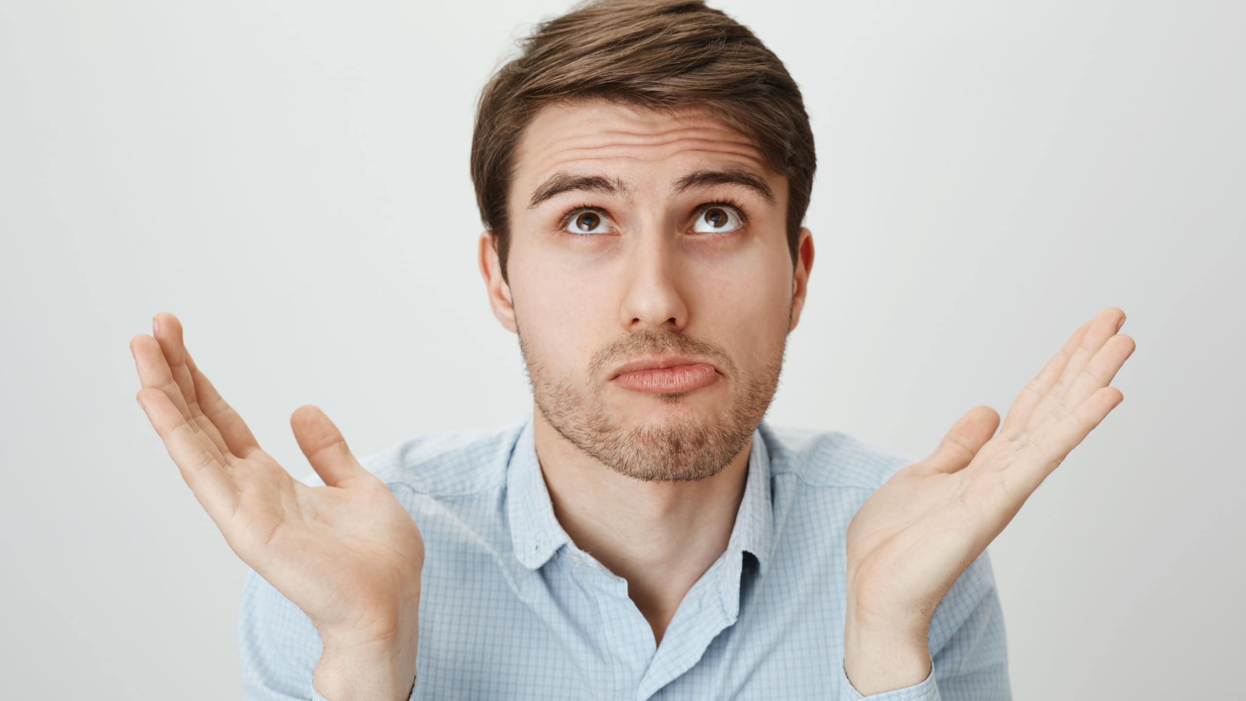 I am not involved, this hands are pure. Indoor portrait of handsome confused guy shrugging with raised palms, looking up and puckering as if making mistake and having no clue how to fix it