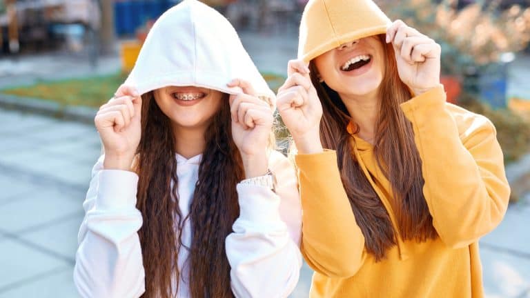 two young girls walking city having fun. joyful Women in bright colored hoodies walking, laughing and posing on the street, pulling the hoods over the heads