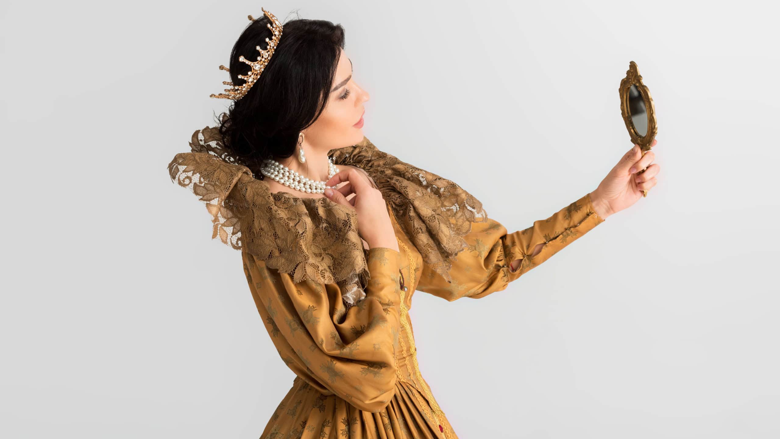 side view of queen with crown looking at mirror isolated on grey