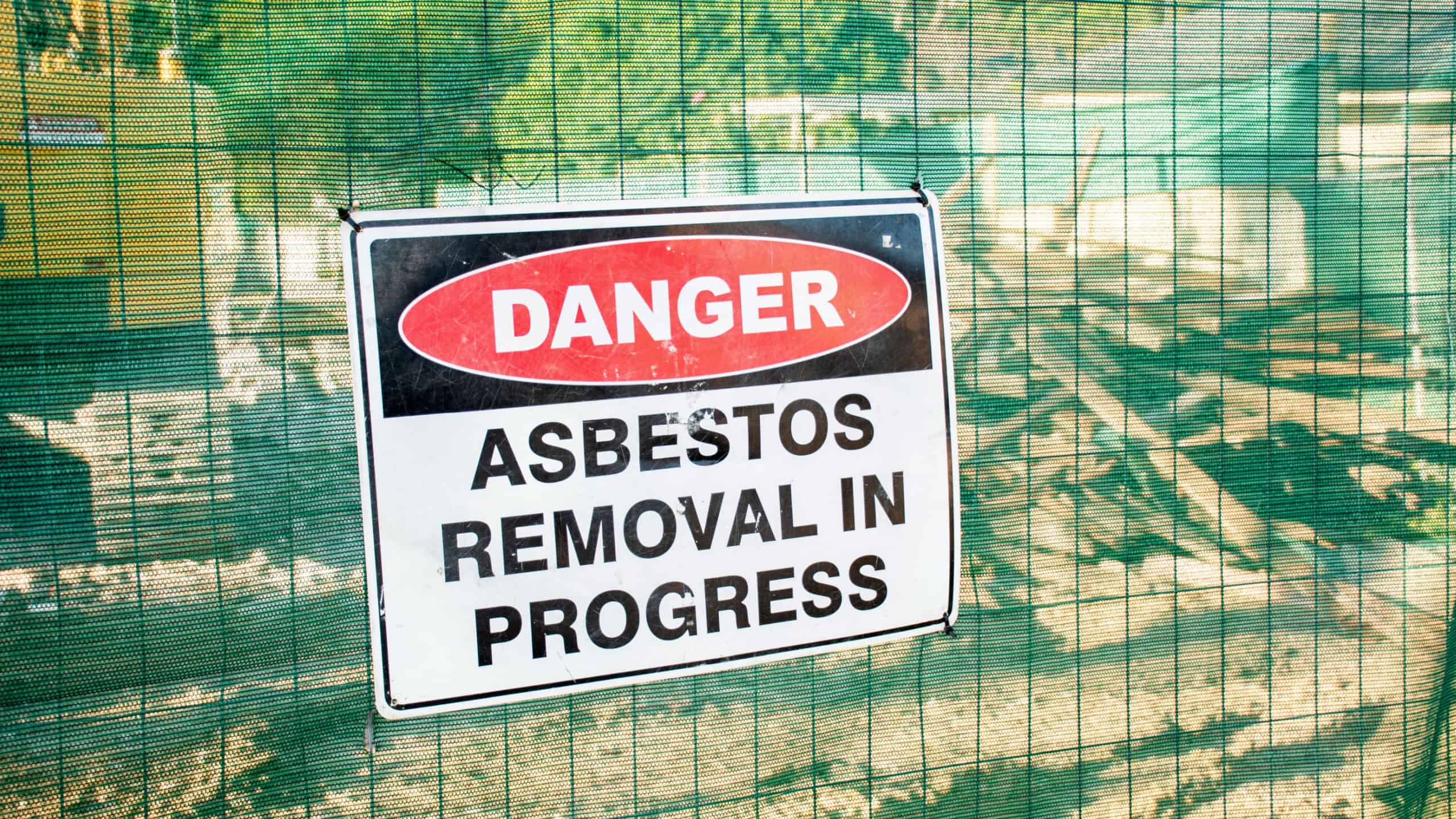A warning sign Danger Asbestos on a fence at construction site where old house is demolishing