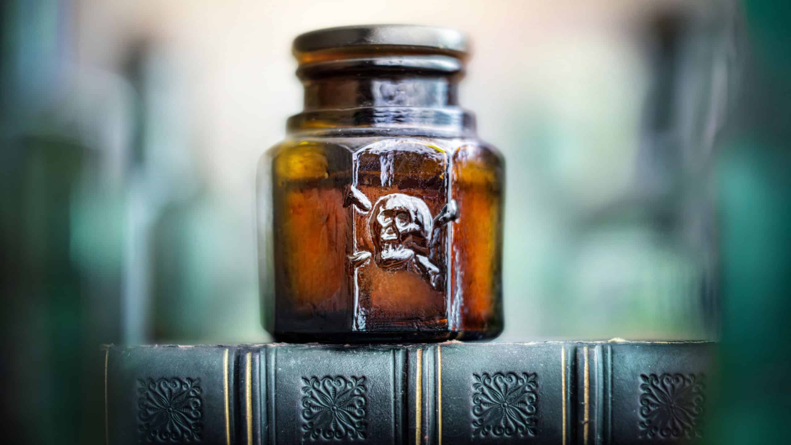 Glass poison bottle with skull and bones. Danger sign, symbol of death. Concept background on poison poisoning, pharmaceutical, chemistry, medical, old science topic.