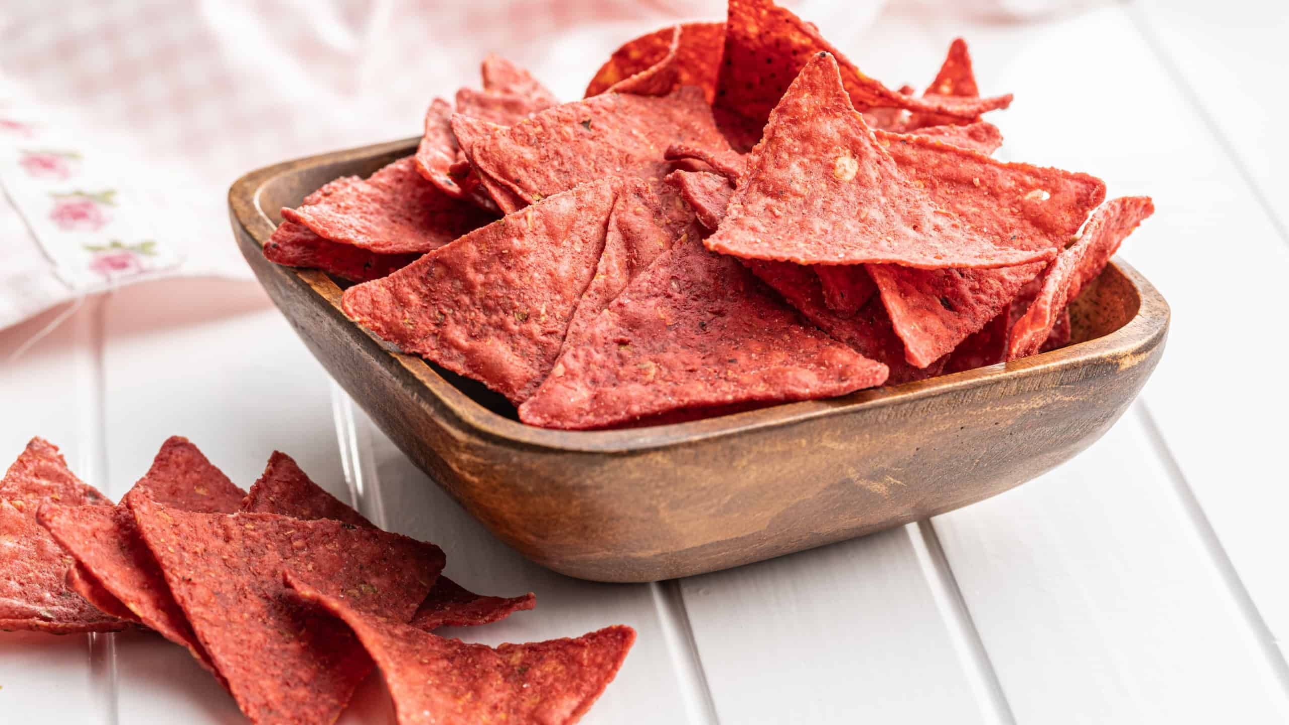 Salted tortilla chips triangle with red beet flavor in bowl on white table.