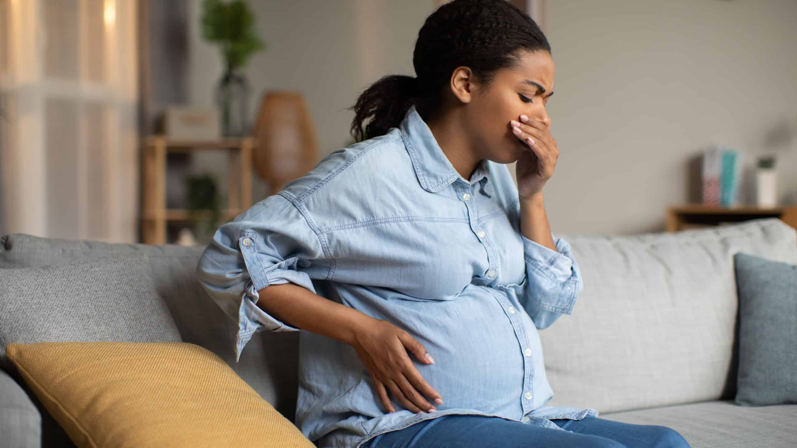 Pregnancy Morning Sickness. Pregnant Black Lady Suffering From Nausea Holding Hand Near Mouth Feeling Bad Sitting On Sofa At Home. Healthcare Concept. Side View