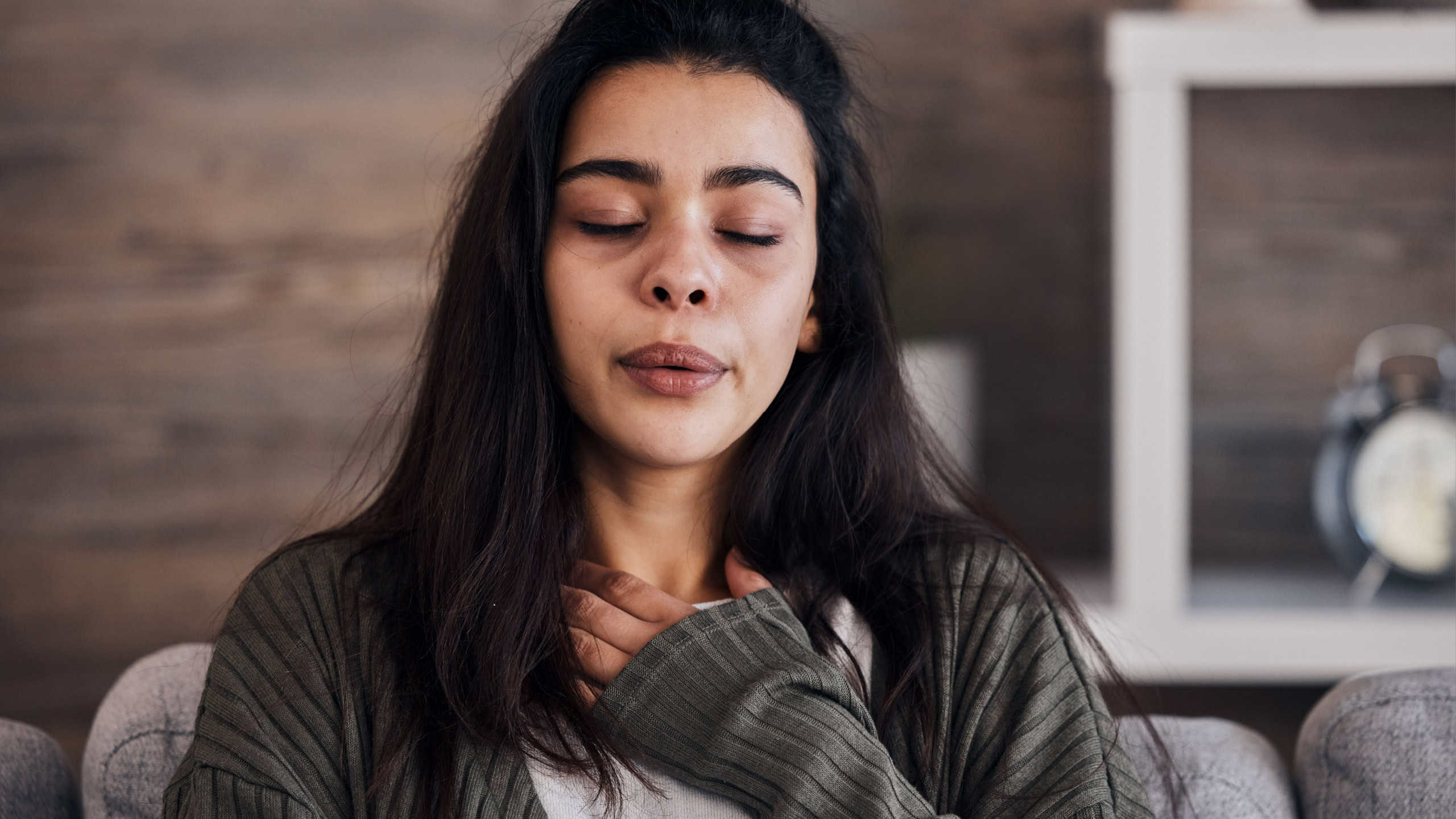 Depression, sad and woman with eyes closed in home thinking of problems. Anxiety, mental health and unhappy, depressed and lonely female on sofa in living room trying to calm down and relax in house.