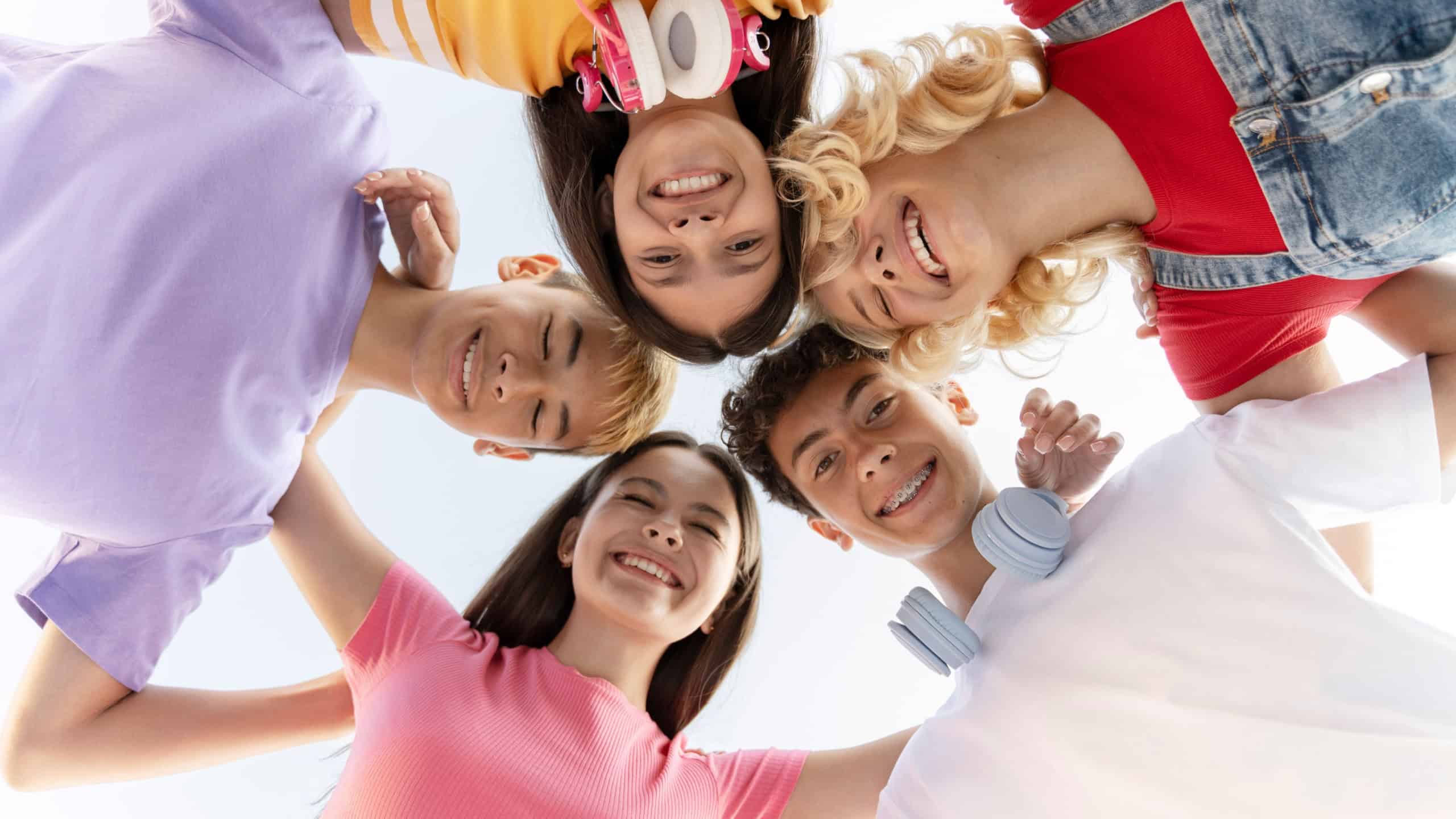 Group of smiling multiracial teenagers hugging, looking at camera outdoors. Portrait of happy friends wearing colorful casual t shirts having fun on the street. Friendship, summer, positive lifestyle