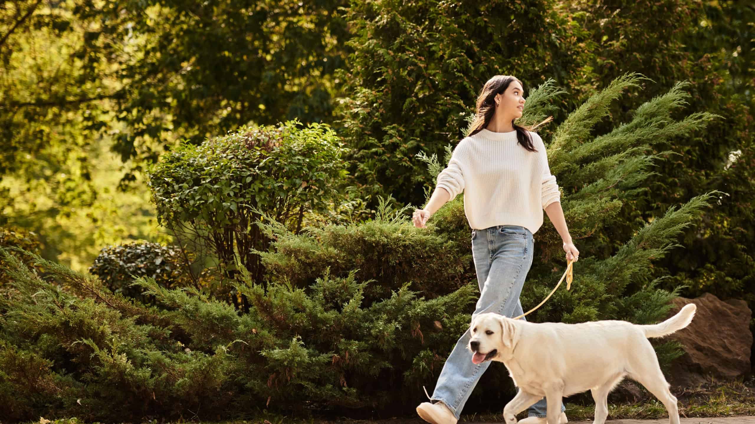 A young woman in cozy autumn attire walks joyfully with her happy dog amidst falling leaves.