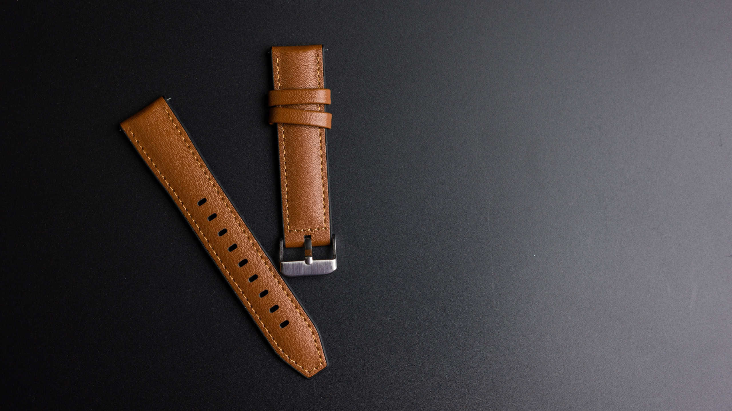 Leather watch strap with buckle on a black background. Top view