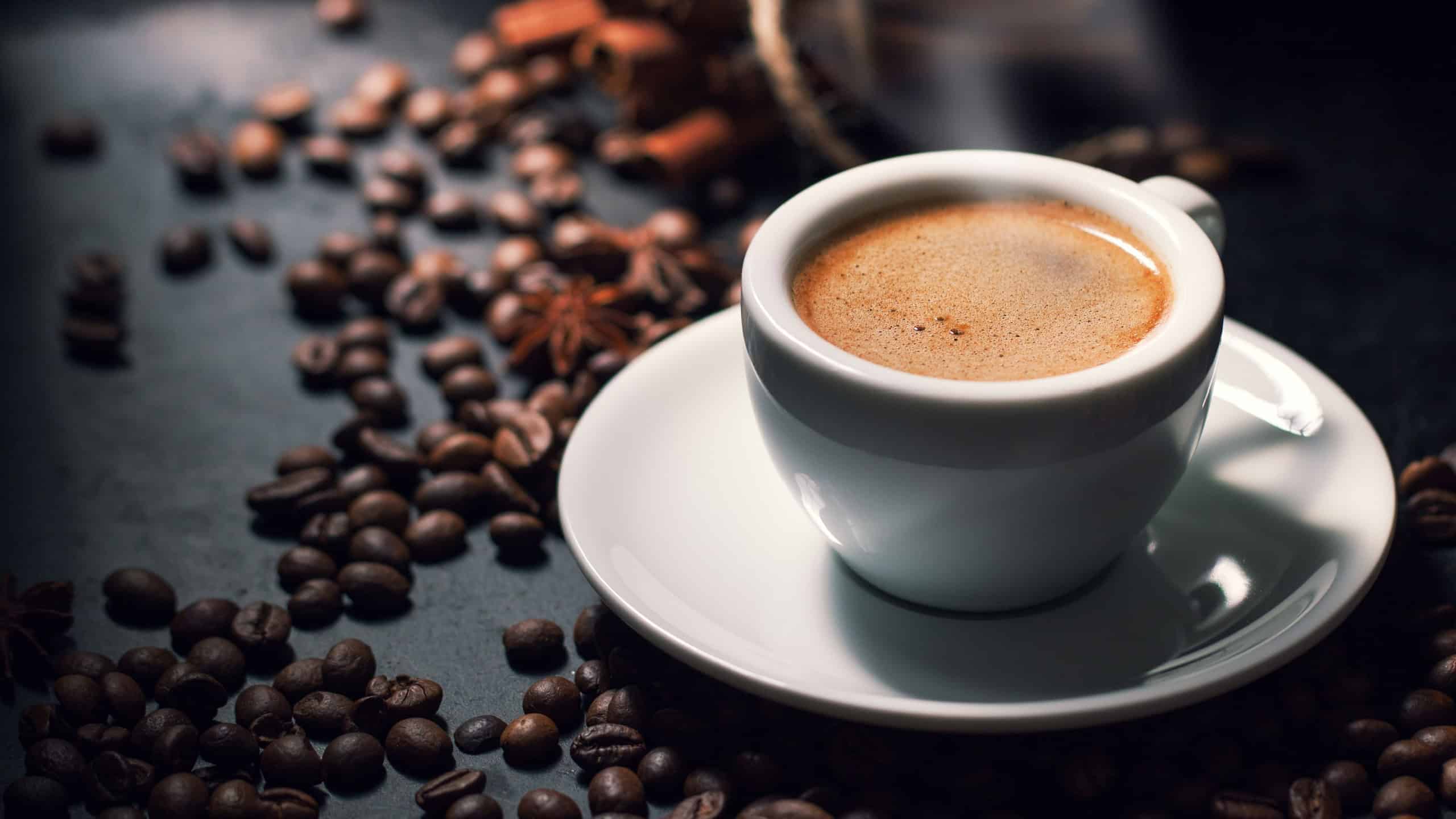 Fresh tasty espresso cup of hot coffee with coffee beans on dark background
