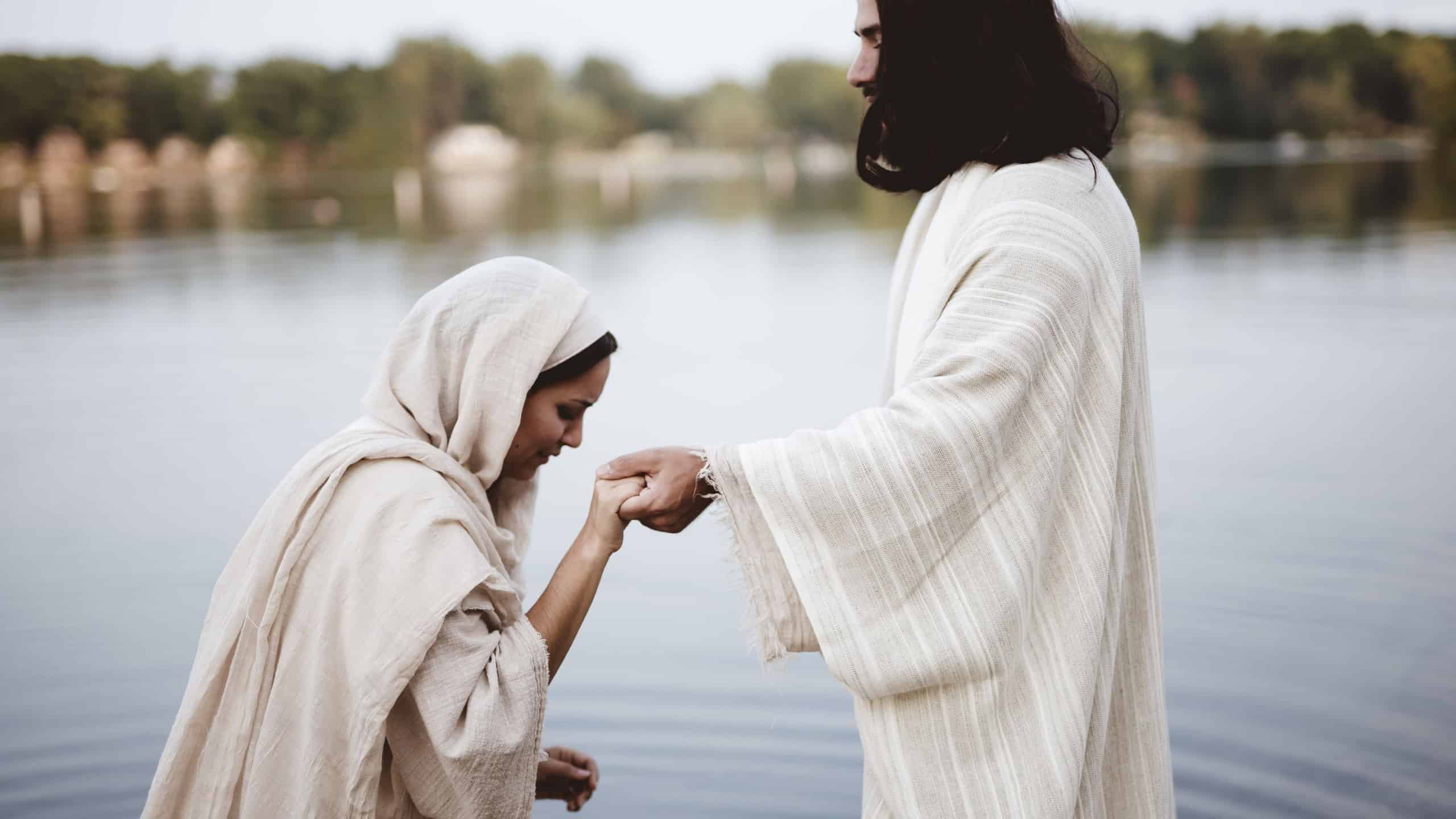A shallow focus shot of a female wearing a biblical gown while holding the hand of Jesus Christ