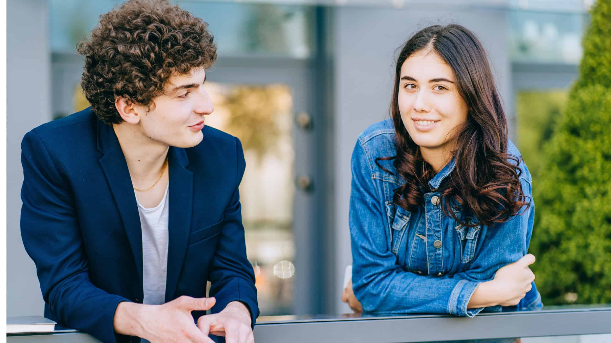 Young diverse students talking during break outdoor over university building, enjoying live communication, multicultural male and female hipster guys discussing, fliring relationship outside.