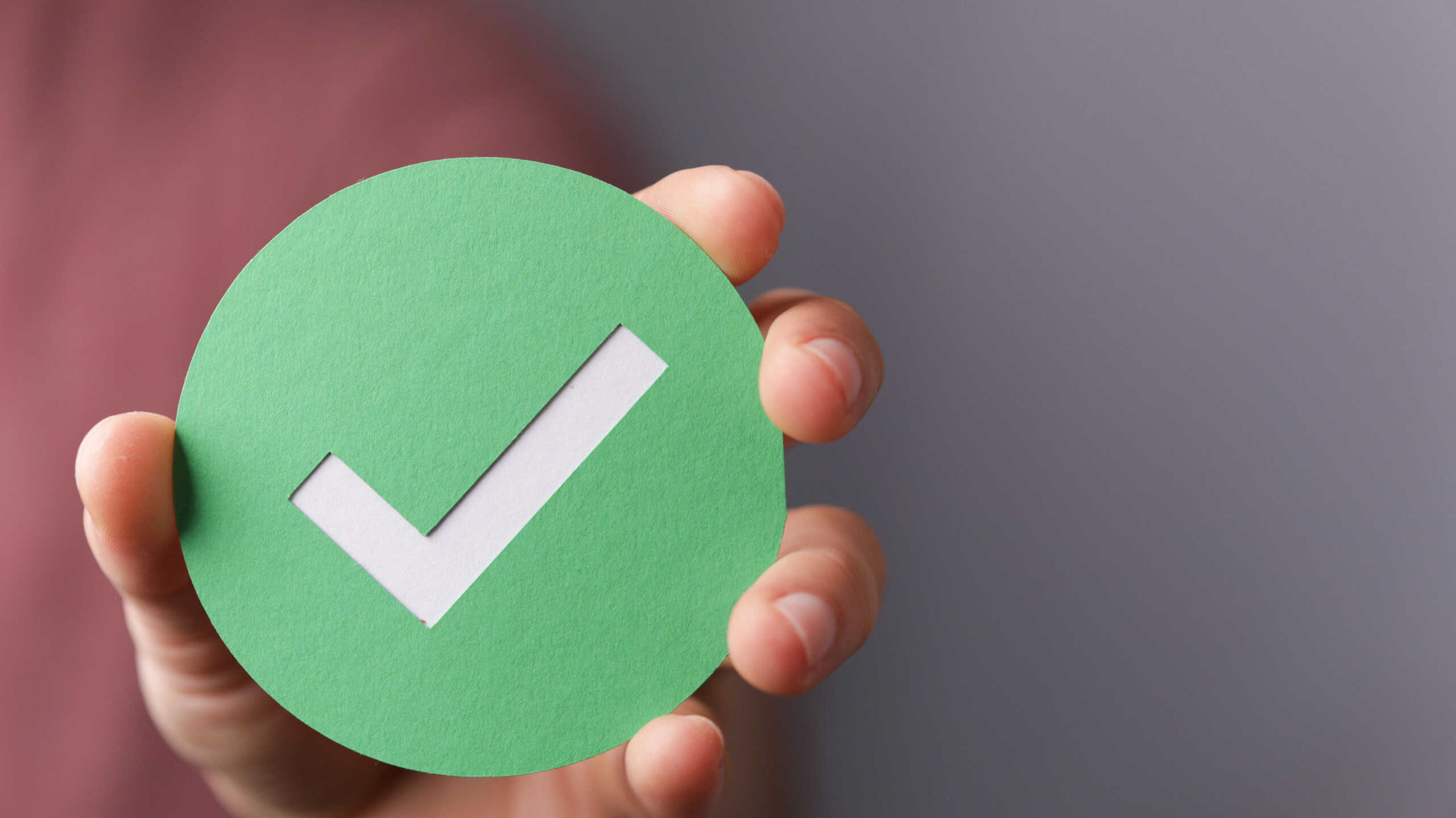 A hand holding a green paper with the checkmark sign on it