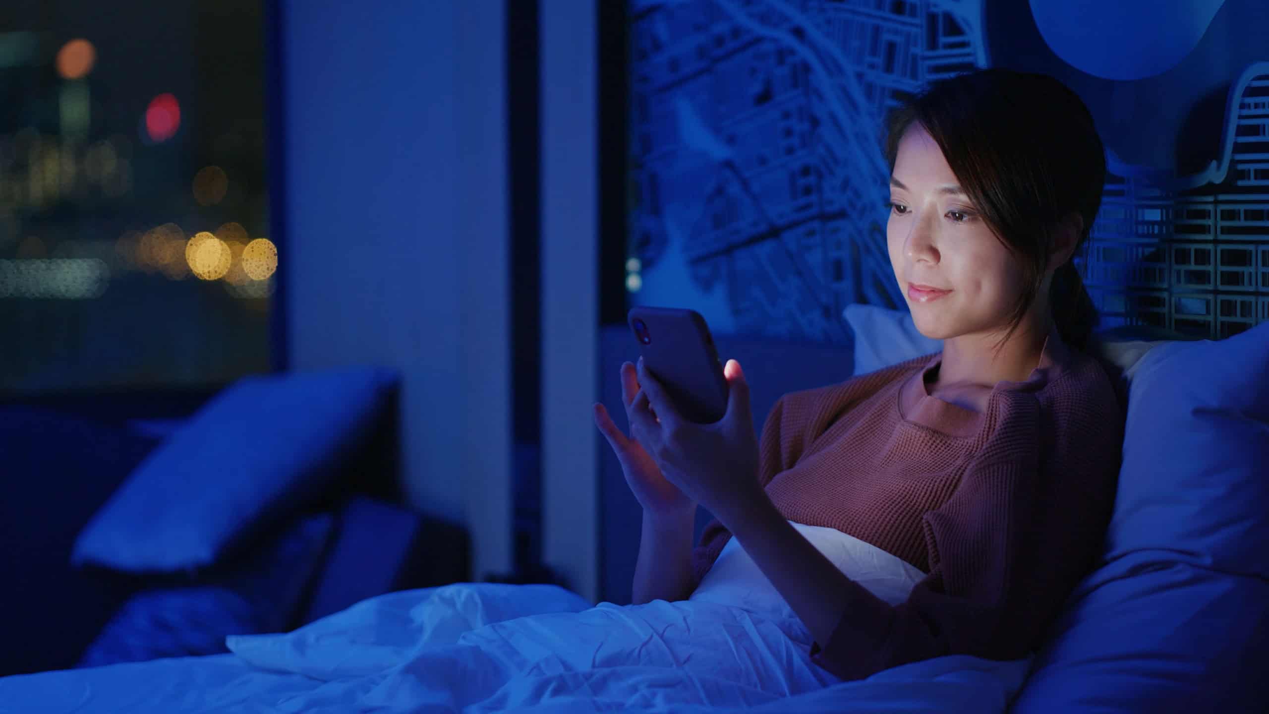 Woman use of mobile phone on bed at night
