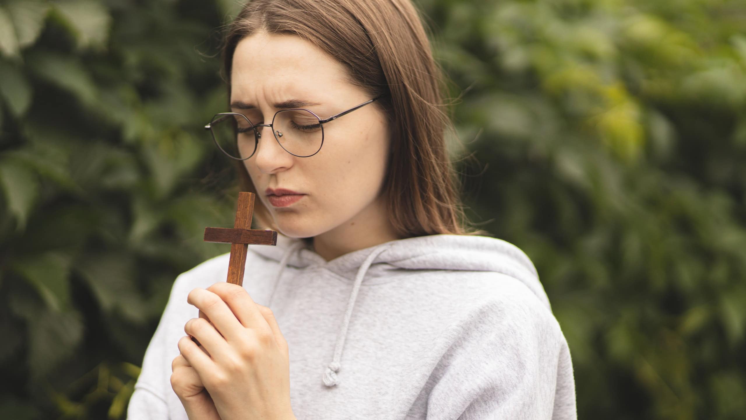 Close-up of hands on the Bible. The process of prayer. The girl holds a wooden crucifix in her hands and prays. Woman's prayer.