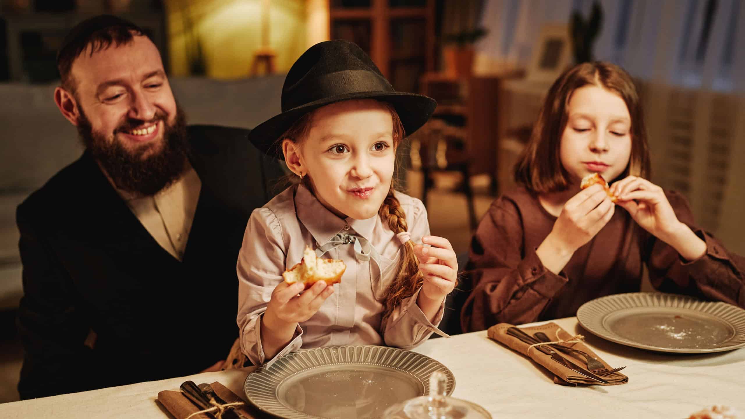 Portrait of happy jewish father with two daughters at dinner table in cozy home setting