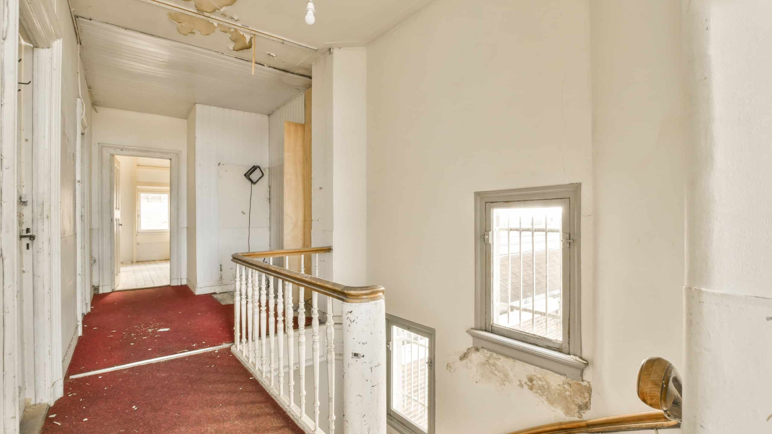 the inside of an old house with red carpet and peeling paint on the walls there is a staircase leading up to the second floor
