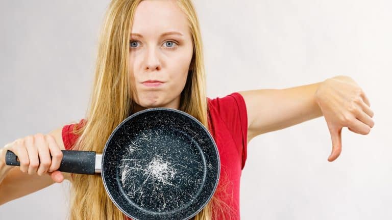 Woman holding scratched frying pan, cause of cancer. Torn coating, kitchen utensil is unusable