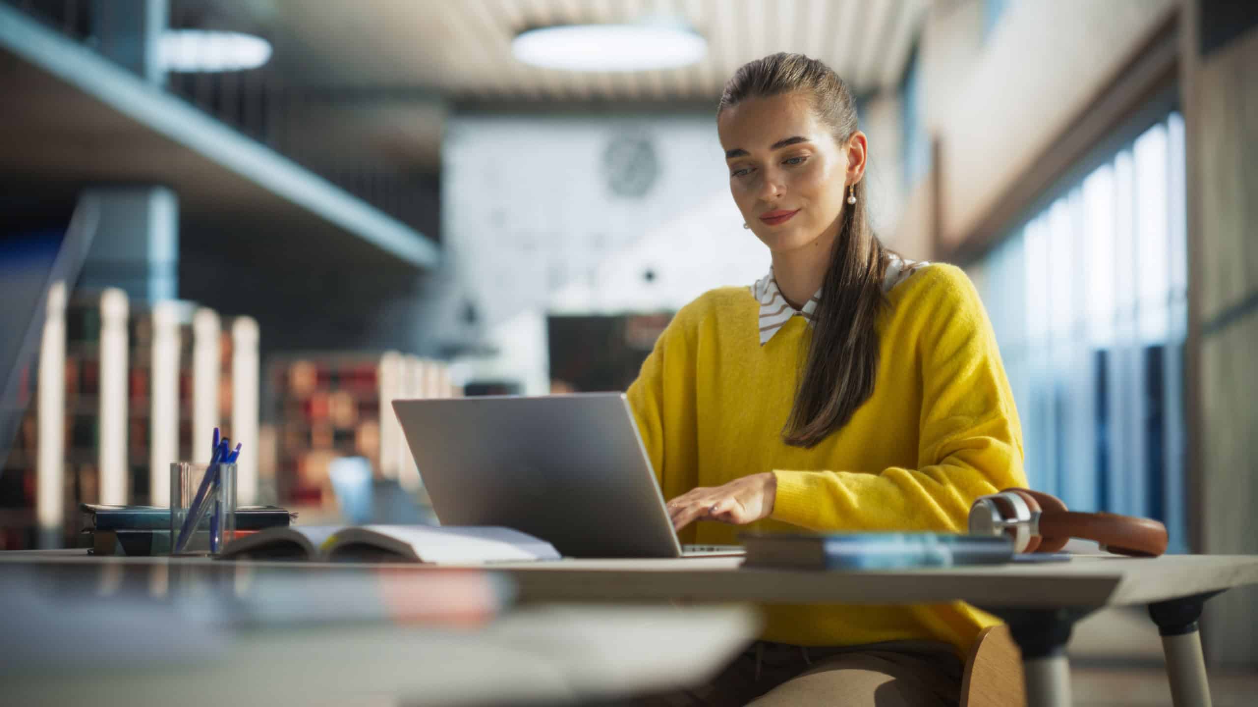 Attractive Multiethnic Student Making a Communication and Journalism Class Homework on a Computer, Researching Answers Online on a Laptop. Young Female Studying in a Public Library