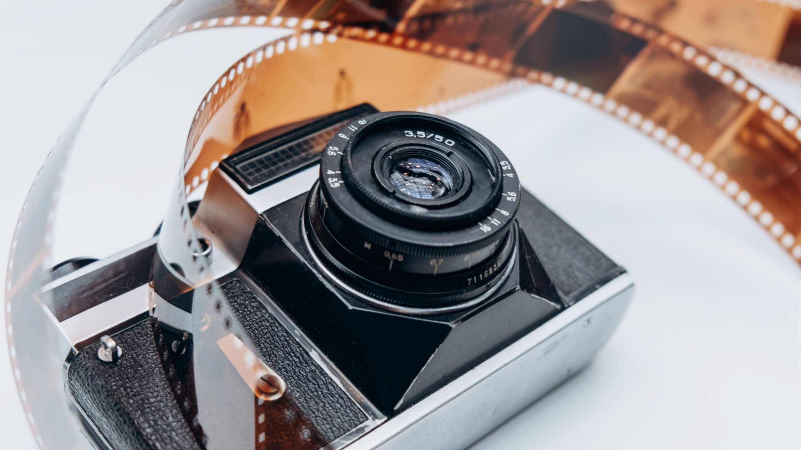 An artistic display of a vintage camera intertwined with a curling film reel, evoking nostalgia for classic photography and film.