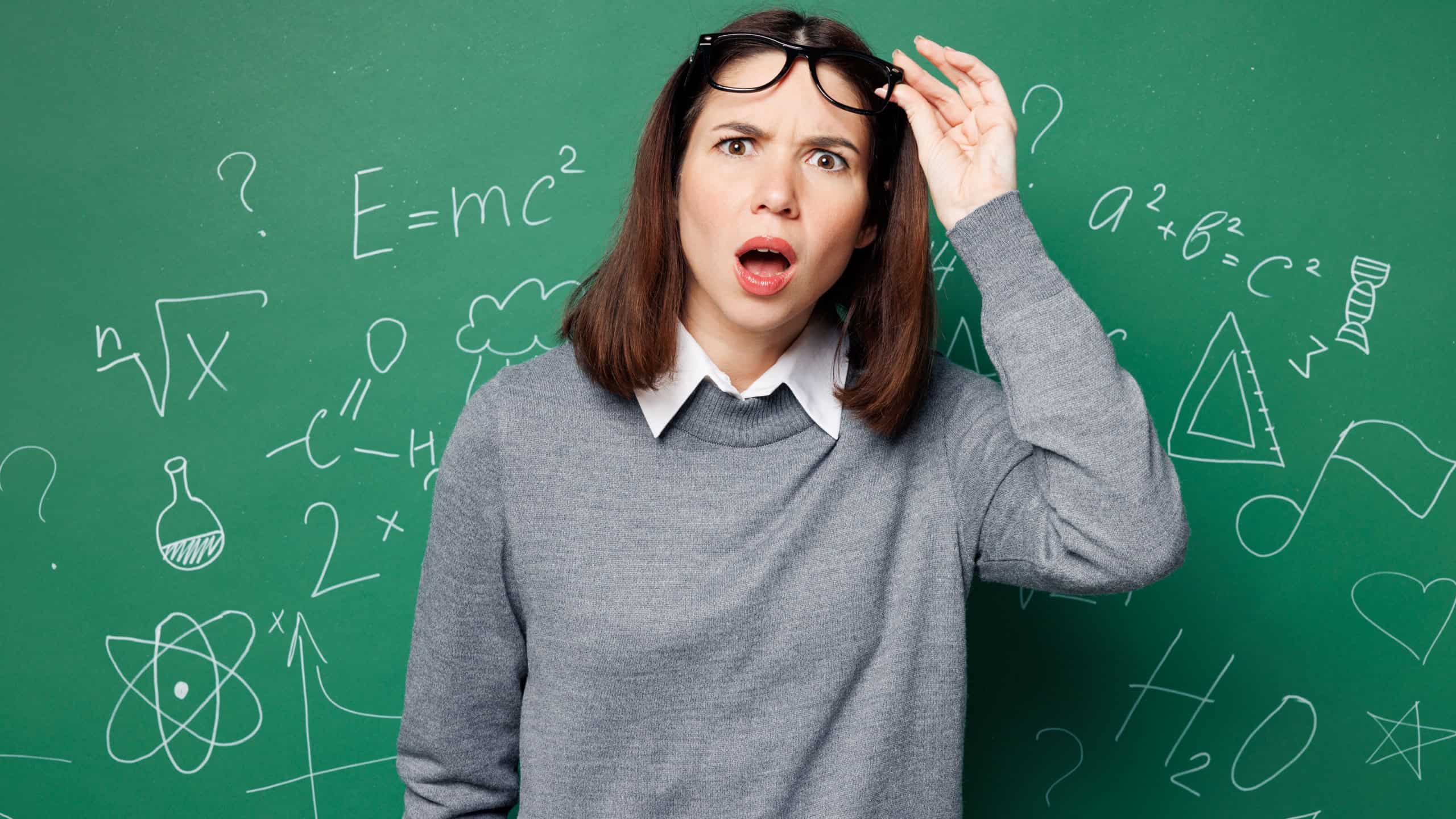 Young shocked mad sad furious smart teacher woman wear grey casual shirt touch glasses look camera isolated on green wall chalk blackboard background studio. Education in high school college concept