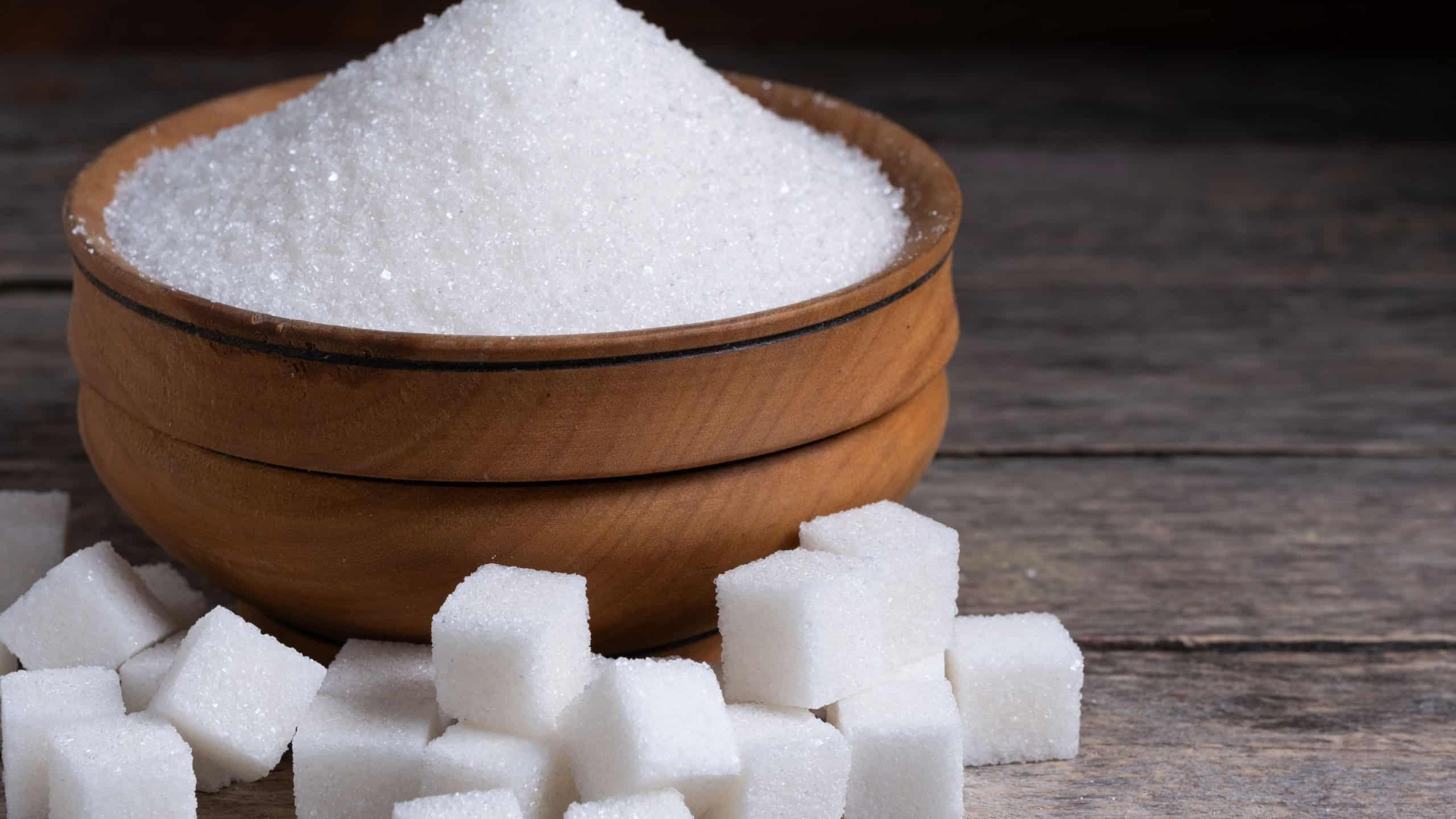 Granulated sugar in a wooden cup, a scattering of refined sugar cubes