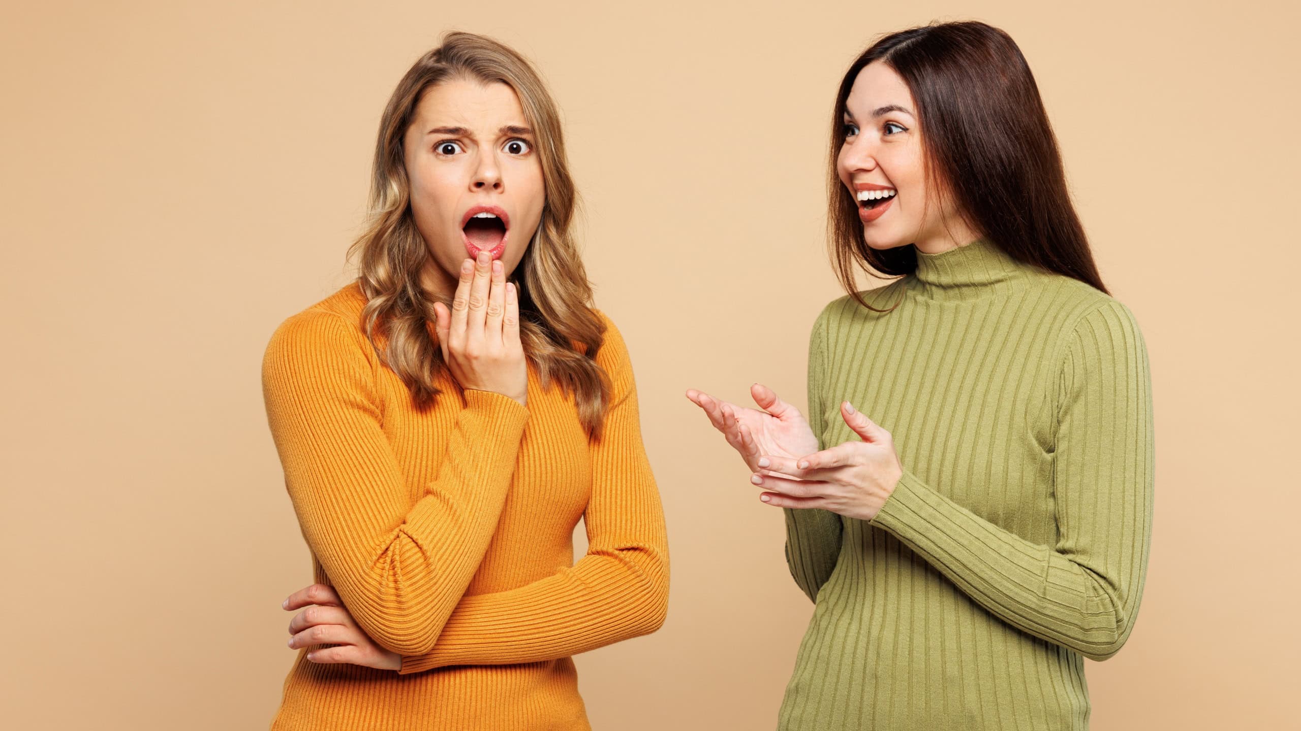 Young friends two women they wear orange green shirt casual clothes together tell secret gossip cover mouth with hand isolated on plain pastel light beige background studio portrait Lifestyle concept2
