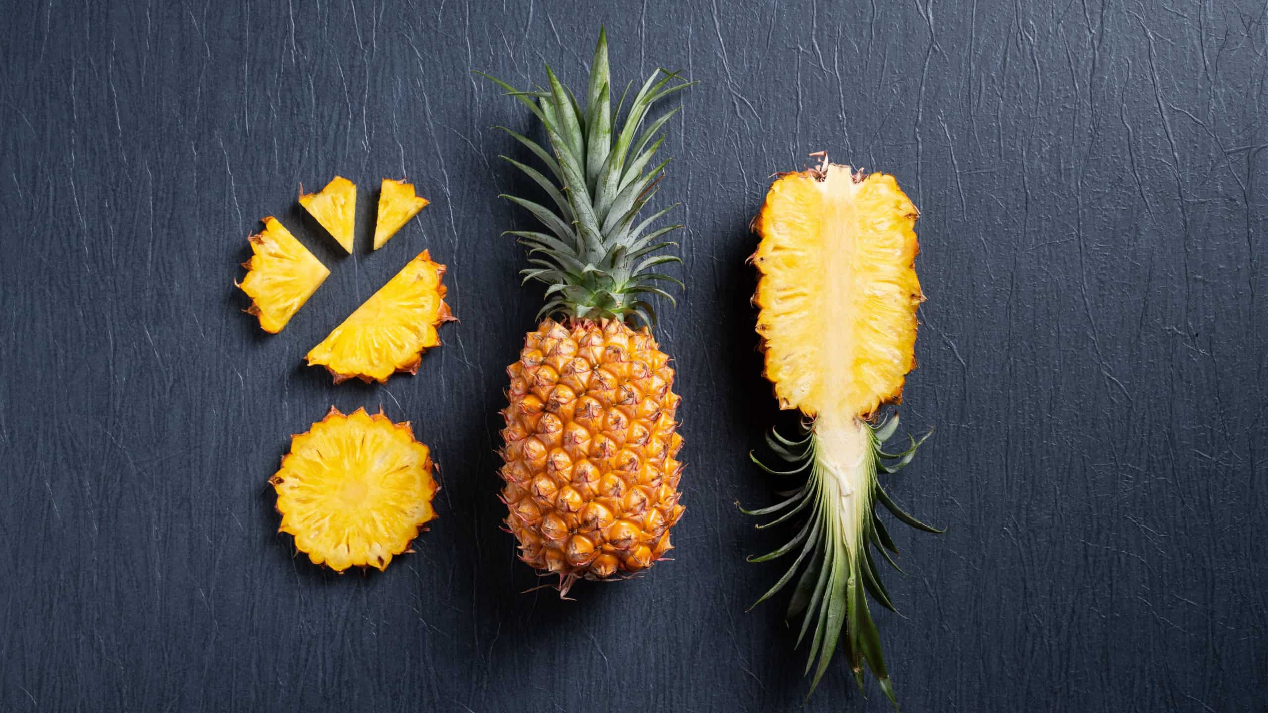 Top view of fresh cut pineapple with tropical leaves on dark blue background.