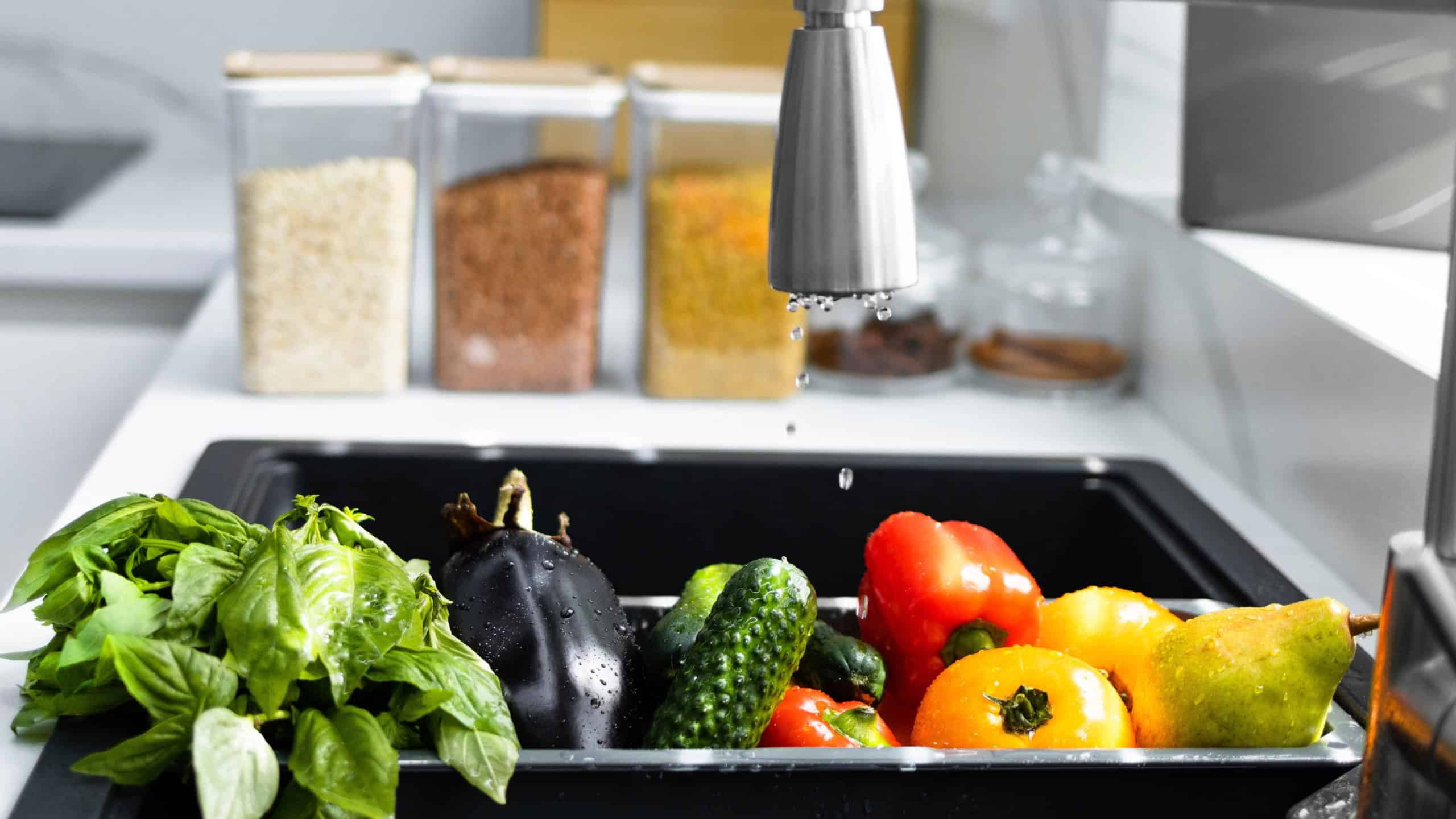 Fresh vegetables and fruits are washed in a special tray for vegetables. Drops of water are poured on the vegetables in the sink. Concept of healthy eating and organic food