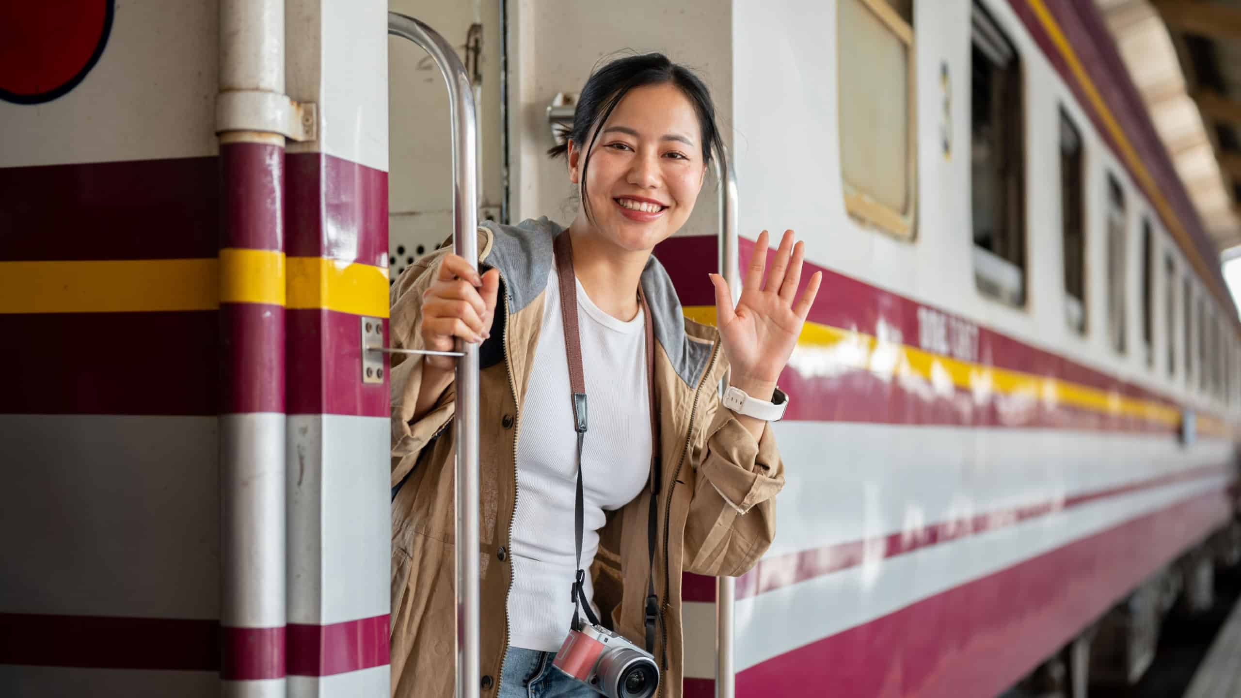 The smiling asian woman is waving her hand while coming down from the carriage at the train station. the vintage train station or railway station.