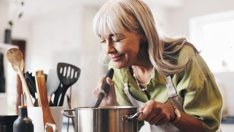Aroma, cooking and mature woman in kitchen in home with smelling dinner, meal or dish. Happy, pot and female person with satisfaction for scent of supper with health, wellness and nutrition in house.