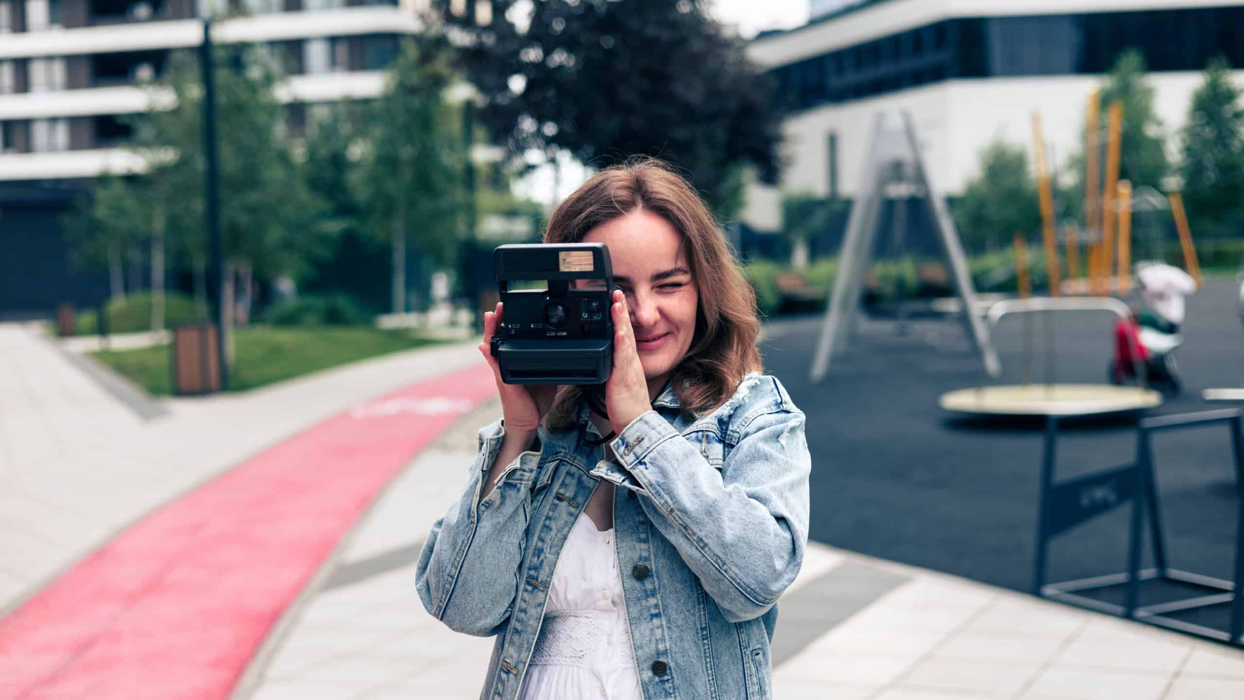Outdoor summer smiling lifestyle portrait of pretty young woman having fun in the city in Europe with retro camera travel photo of photographer taking pictures.