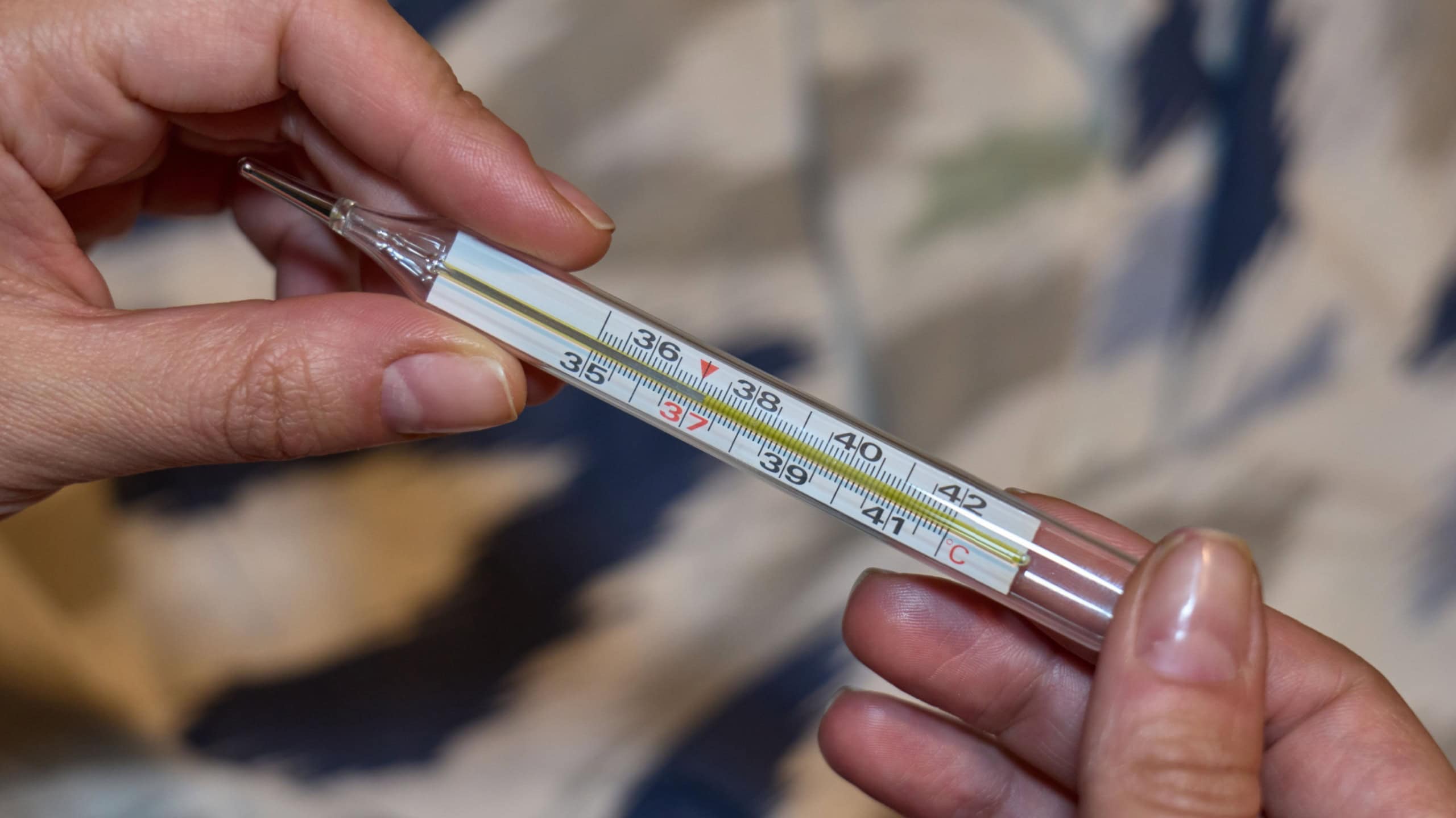 A person holds a mercury thermometer measuring body temperature