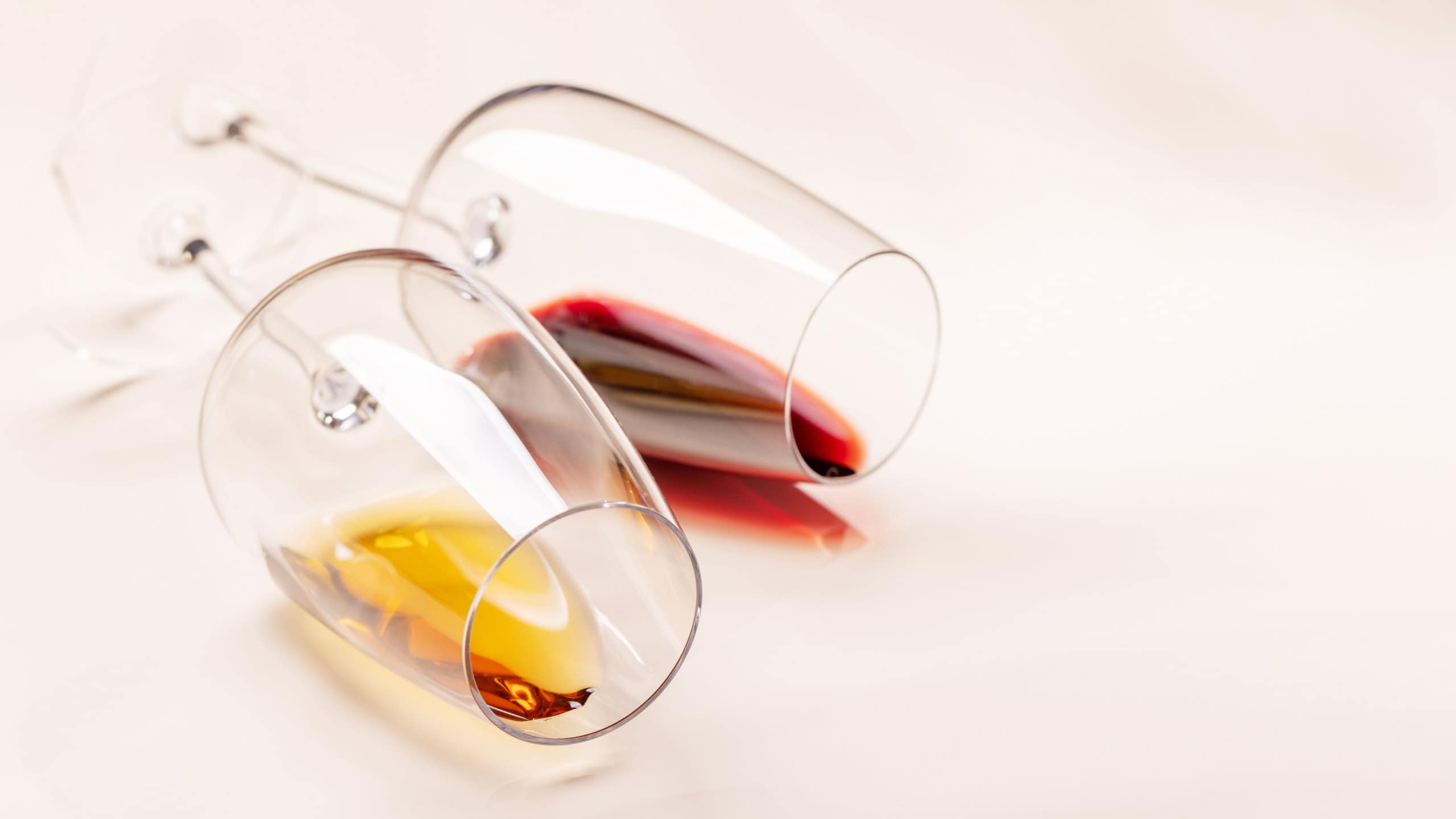 Wine glasses with red and white wine lying on beige background, minimal elegant style