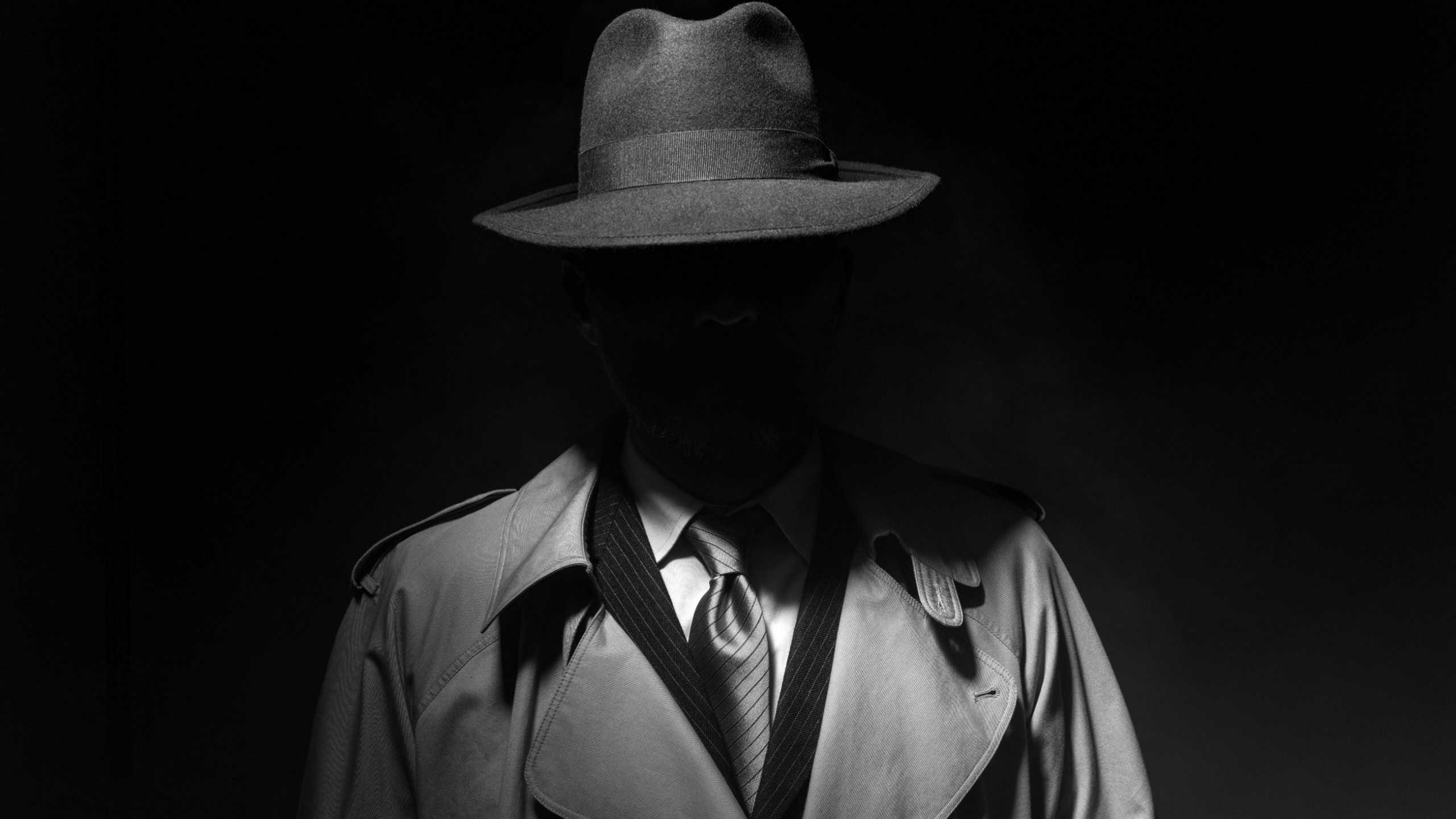 Man posing in the dark with a fedora hat and a trench coat, 1950s noir film style character