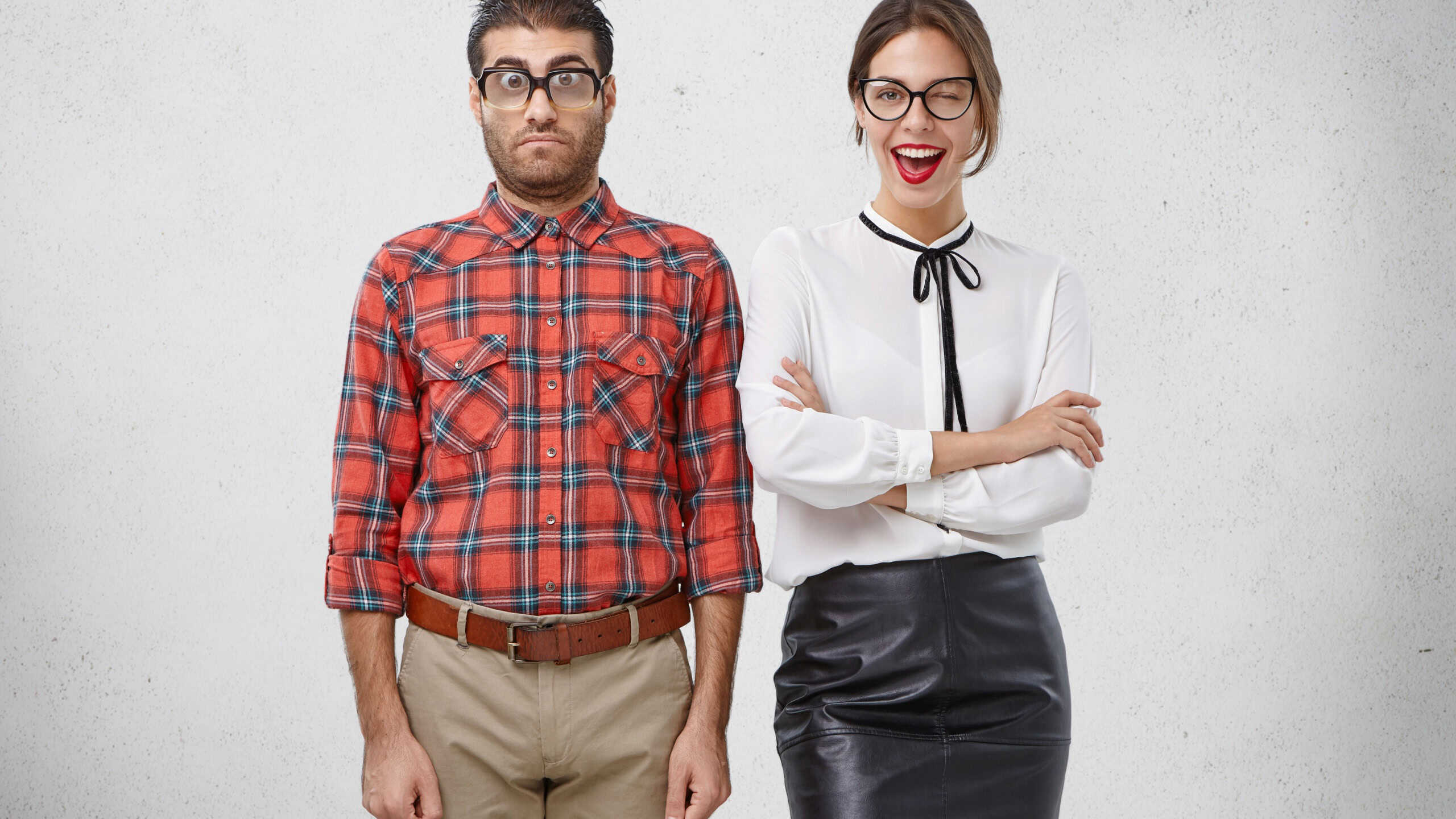 Best friends stand next to each other: unshaven puzzled man in glasses and checkered shirt and beautiful woman winks with eye joyfully, being glad to meet former schoolmate, remember school years