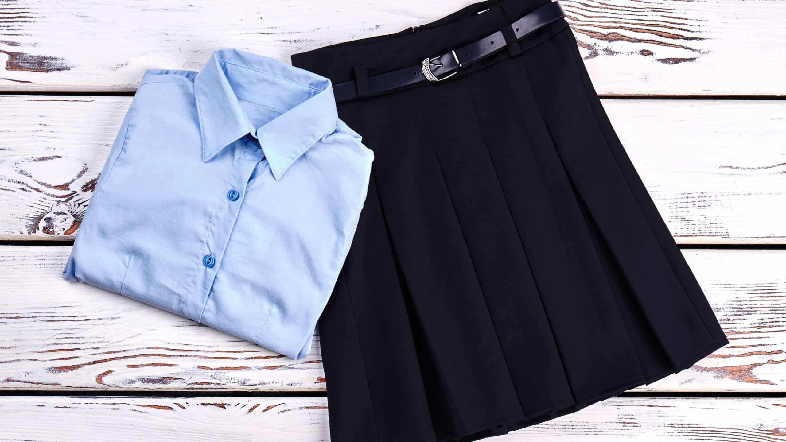Elegant cotton shirt and skirt. Girls new buttoned blue shirt and pleated skirt with belt for school, top view. Girls school uniform on sale.