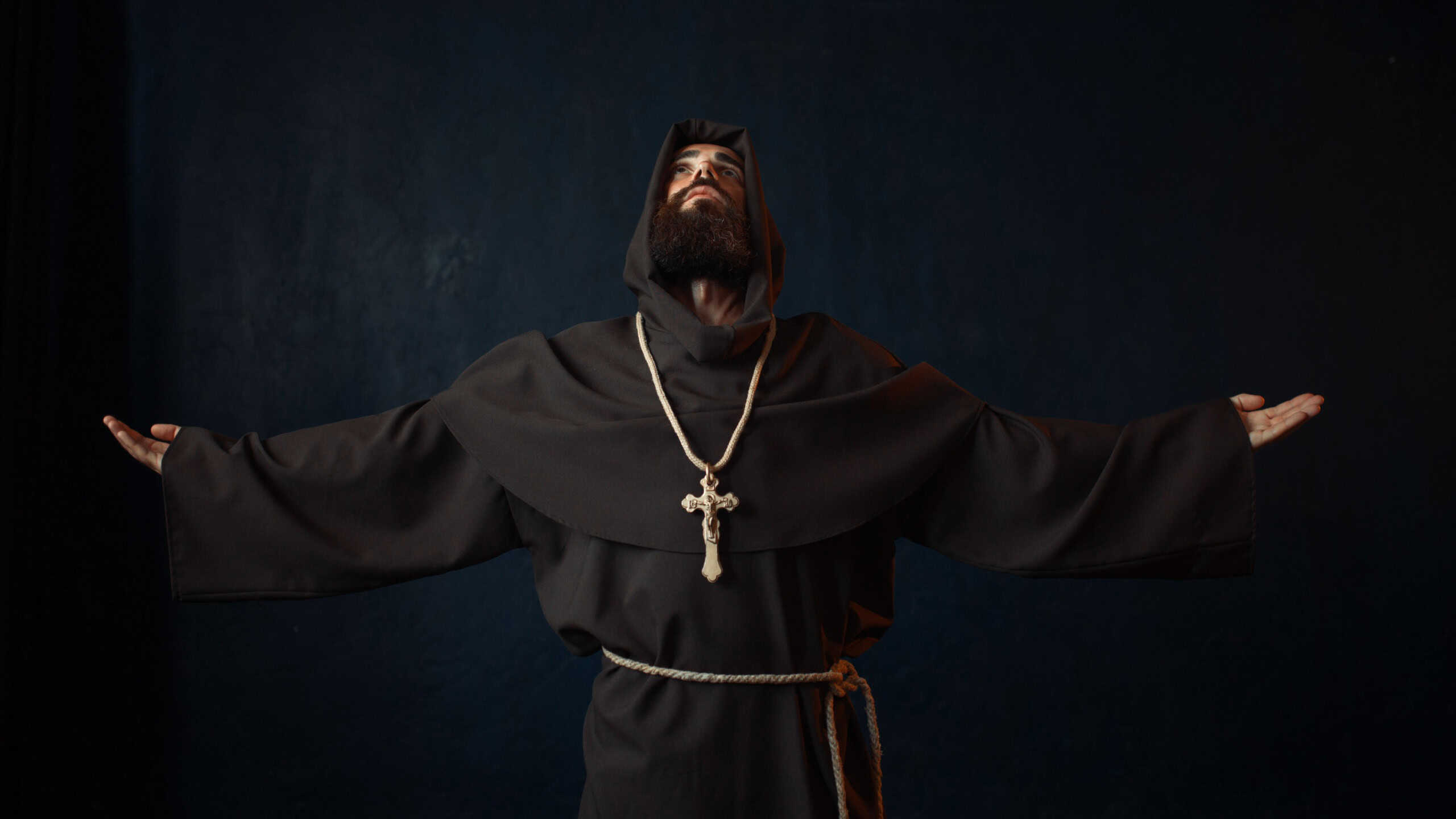 Monk in black robe with hood kneeling and praying