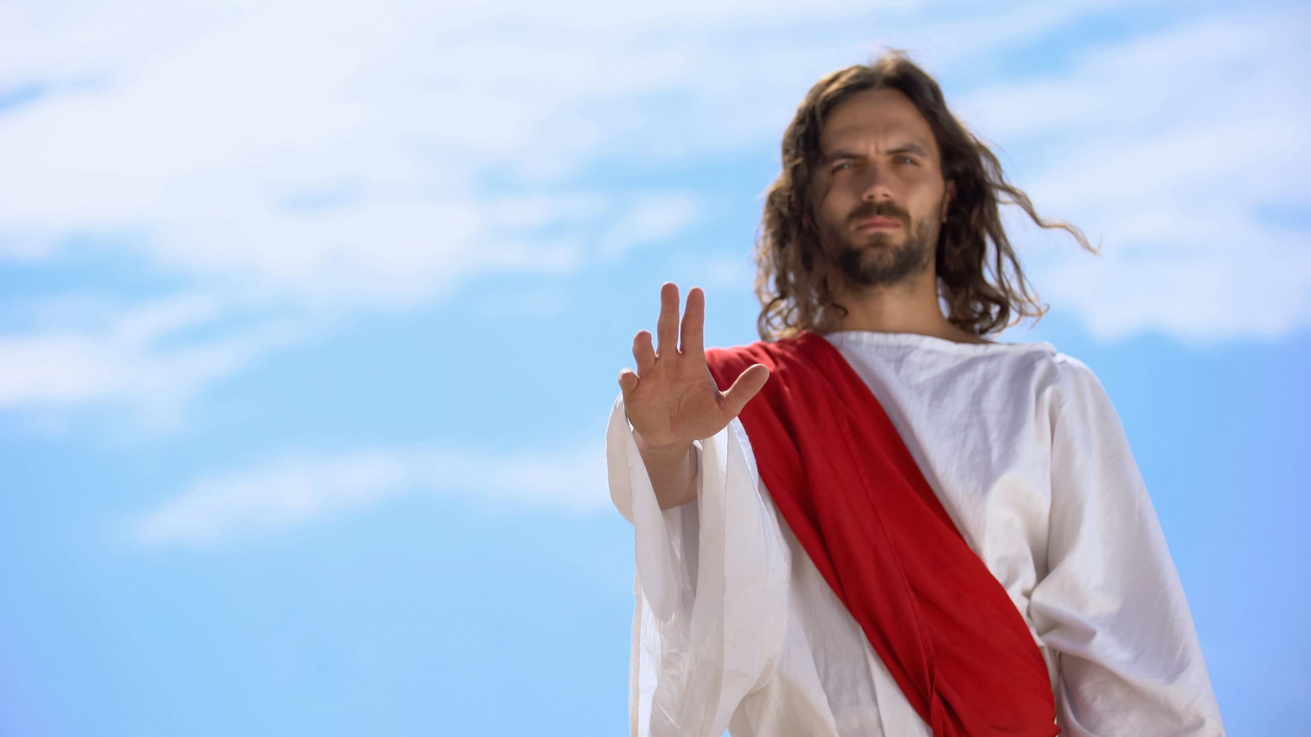 Jesus in robe stretching opened palm on camera, blessing and healing